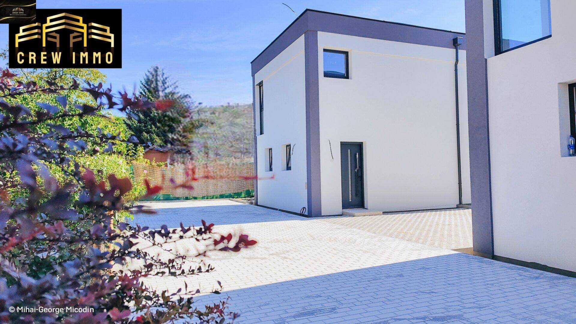 Ansicht eines modernen Einfamilienhauses mit weißer Fassade und dunklen Akzenten unter blauem Himmel.