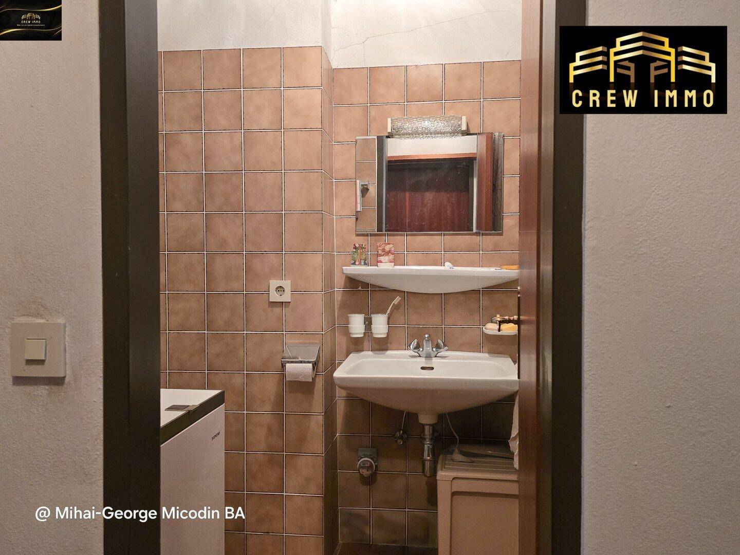 Kleines Badezimmer mit braunen Fliesen, Waschbecken und Spiegel.