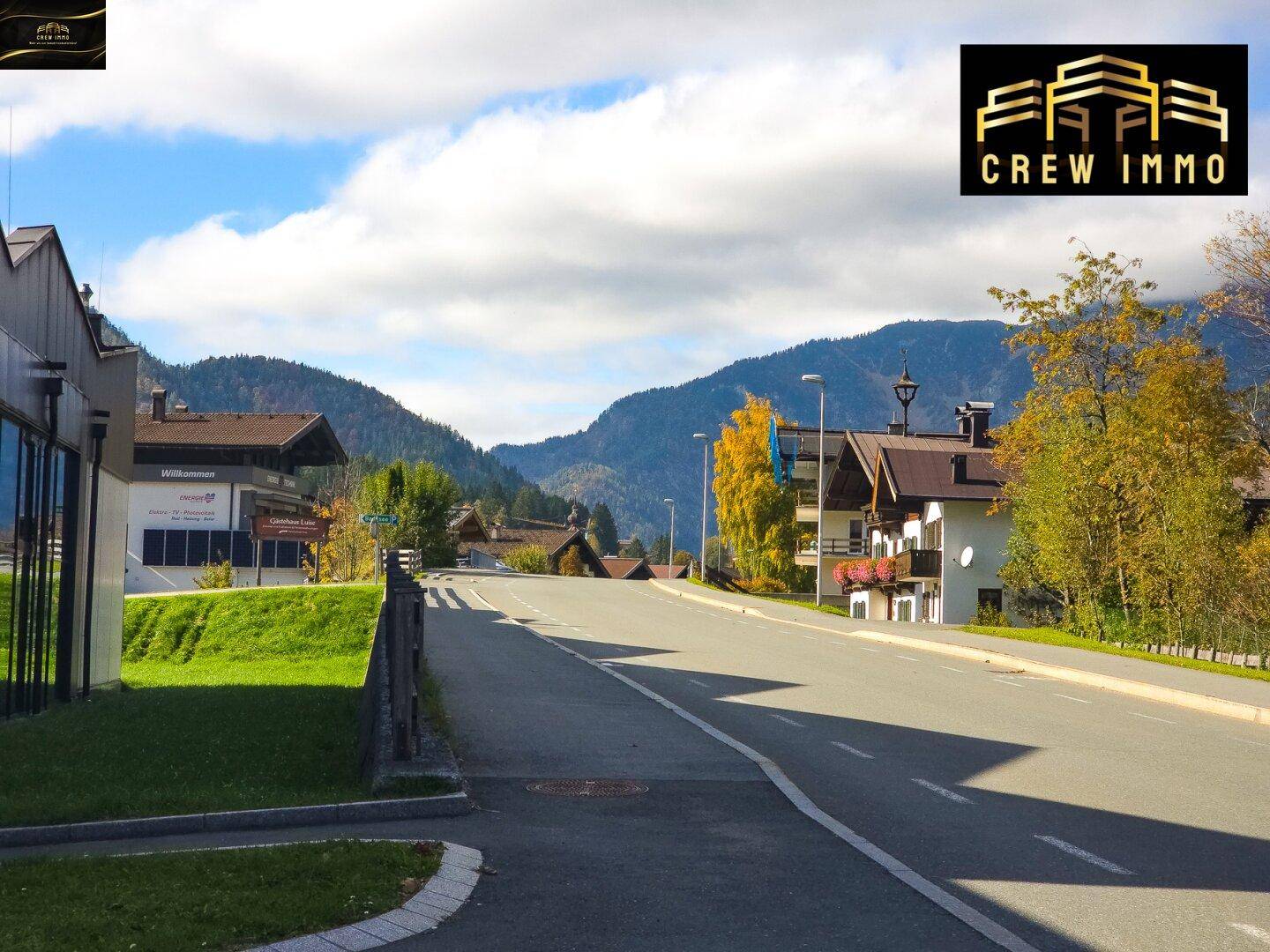 Ruhige Straße in einer alpinen Siedlung mit Häusern und Bergen im Hintergrund.