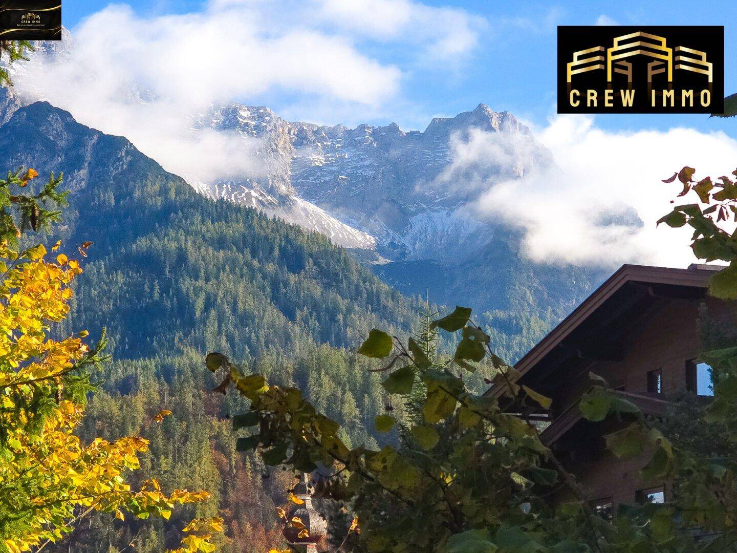 Malerische Berglandschaft mit schneebedeckten Gipfeln und einem traditionellen Haus im Vordergrund.