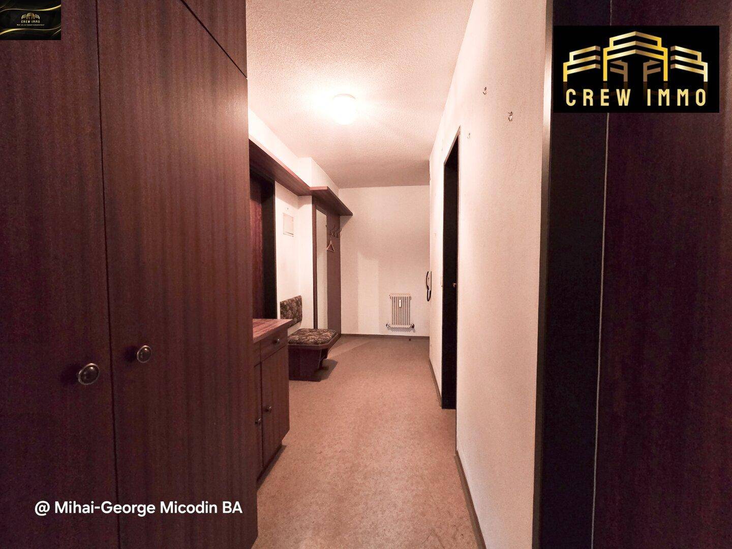 Langer Flur mit Holzschränken, Garderobe und Heizkörper an der Wand.