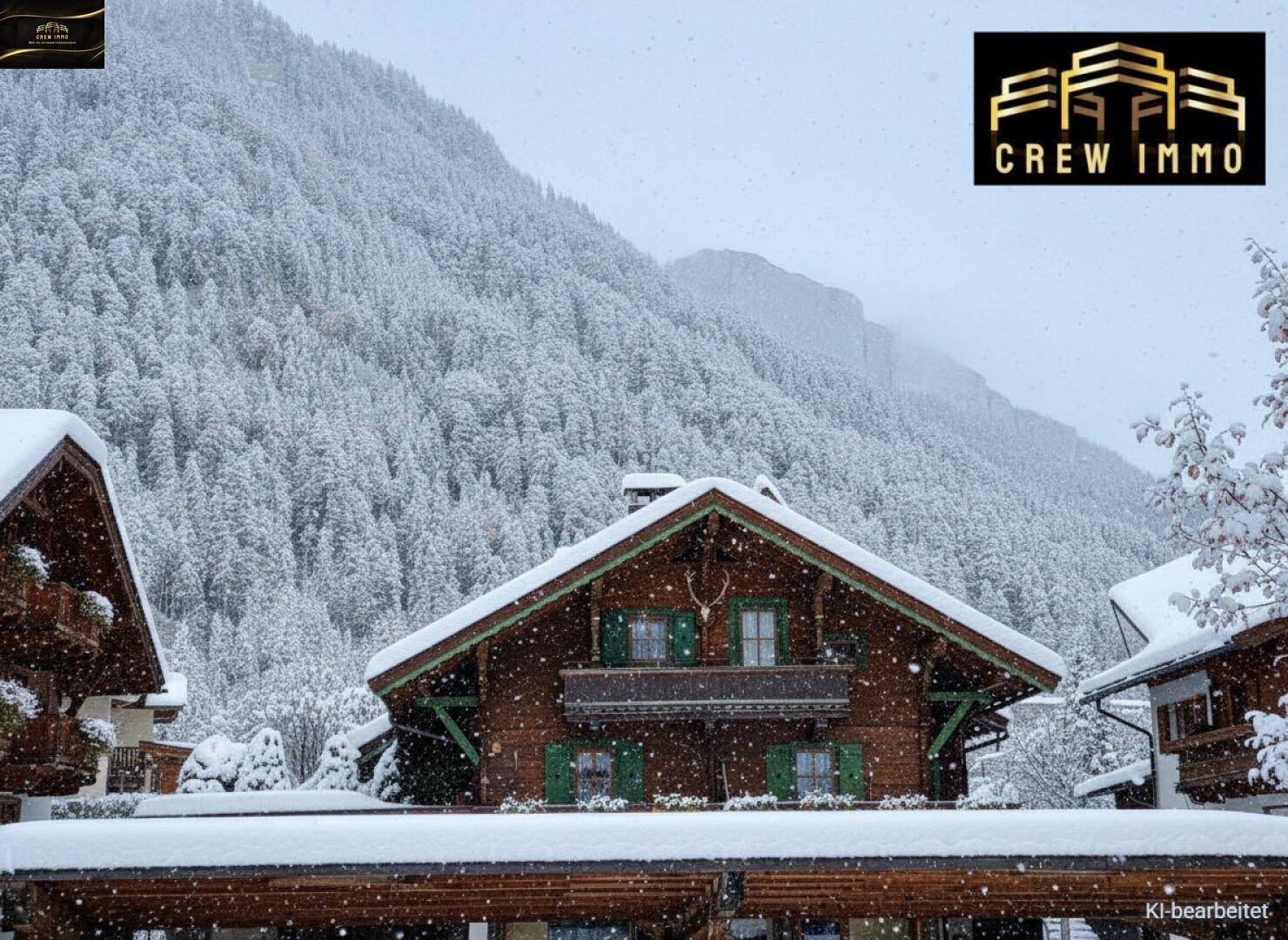 Traditionelles Holzhaus im alpinen Stil, bedeckt mit Schnee, vor einer winterlichen Bergkulisse.