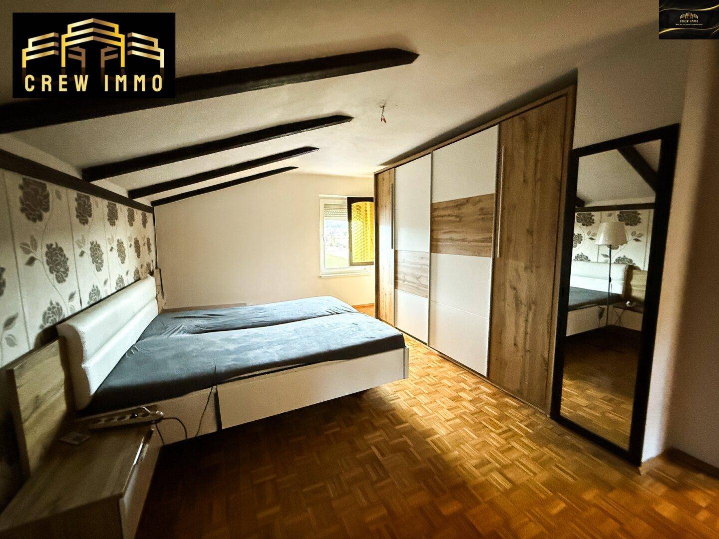 Gemütliches Schlafzimmer mit Holzbalken, Parkettboden und großem Einbauschrank.