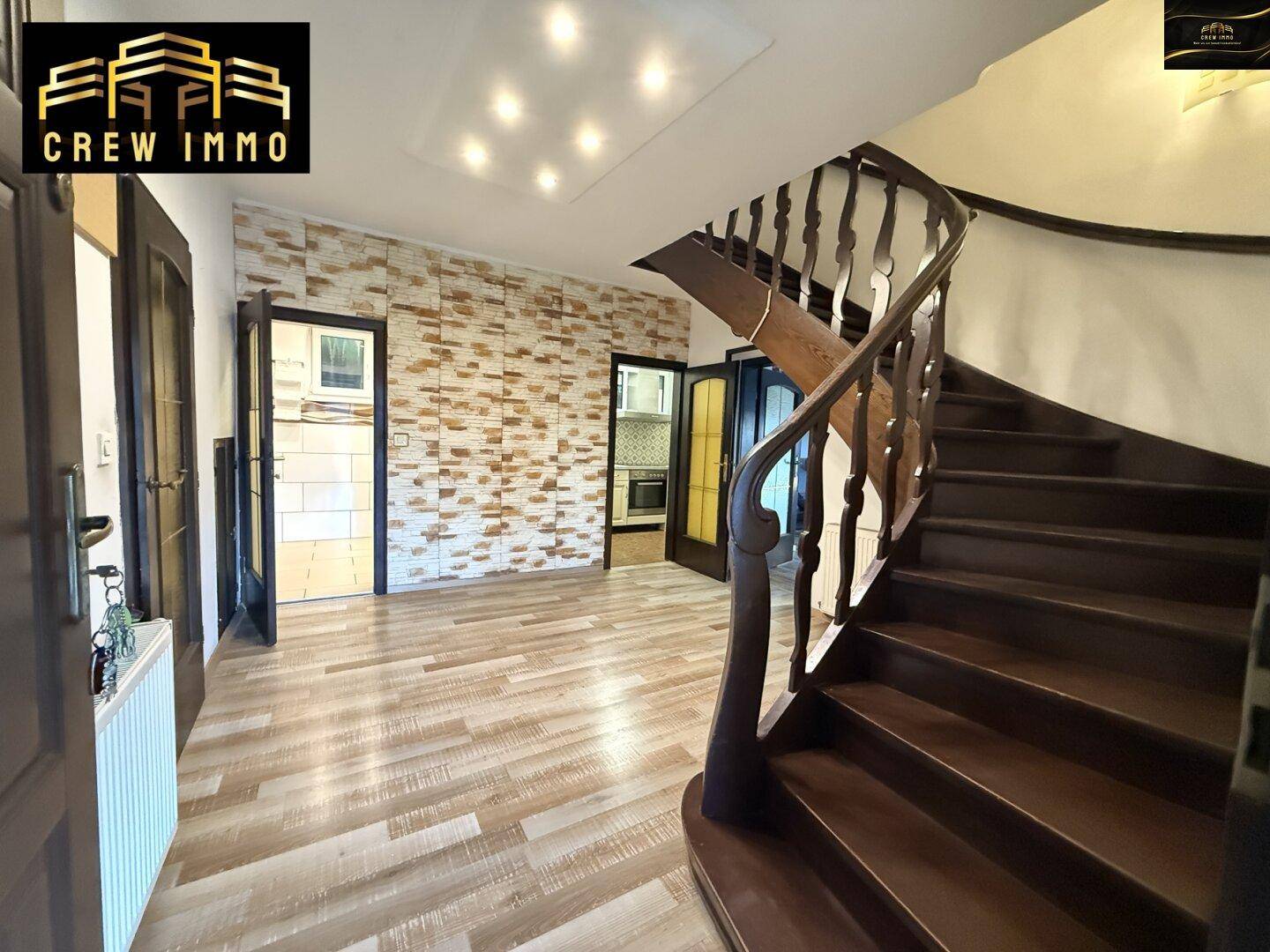 Geräumiger Eingangsbereich mit Holztreppe, Laminatboden und dekorativer Ziegelwand.