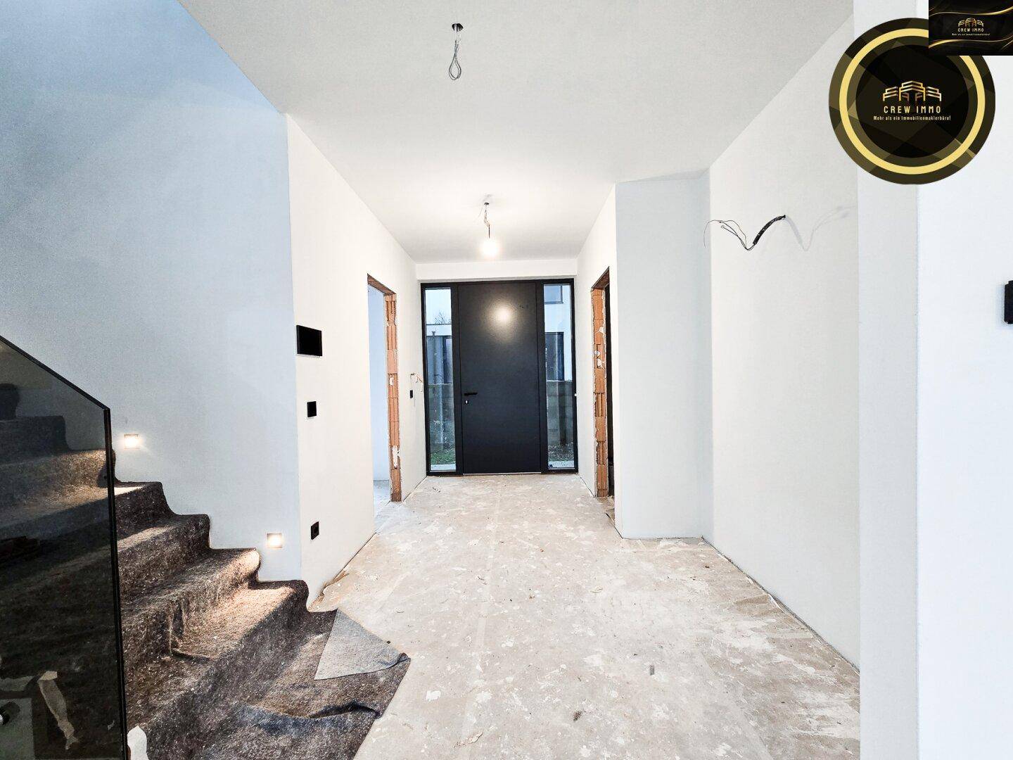 Unfertiger Eingangsbereich mit rohem Boden, weißen Wänden und moderner Treppe.