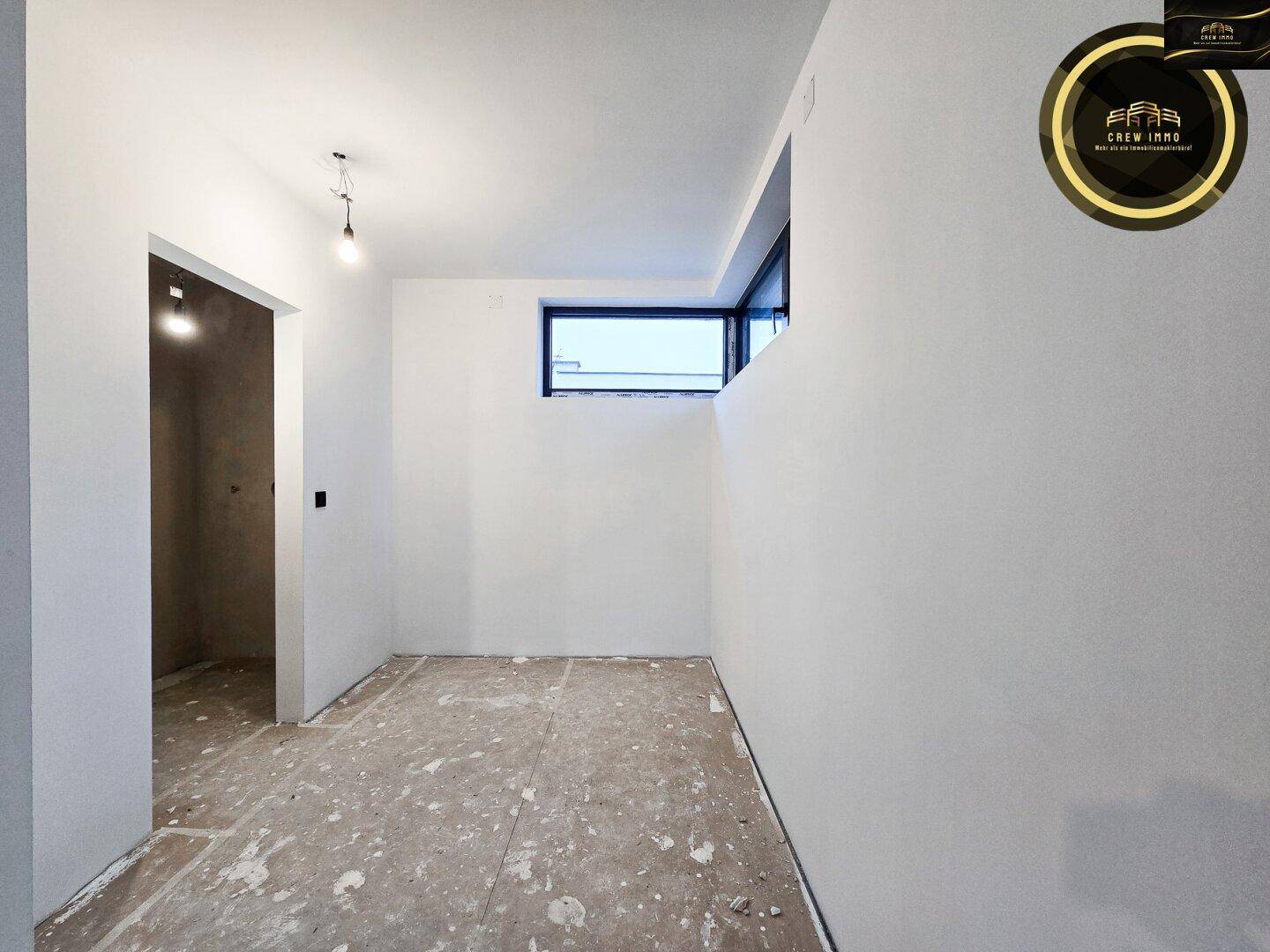 Unfertiger Hauswirtschaftsraum mit kleinem Fenster und rohem Boden.