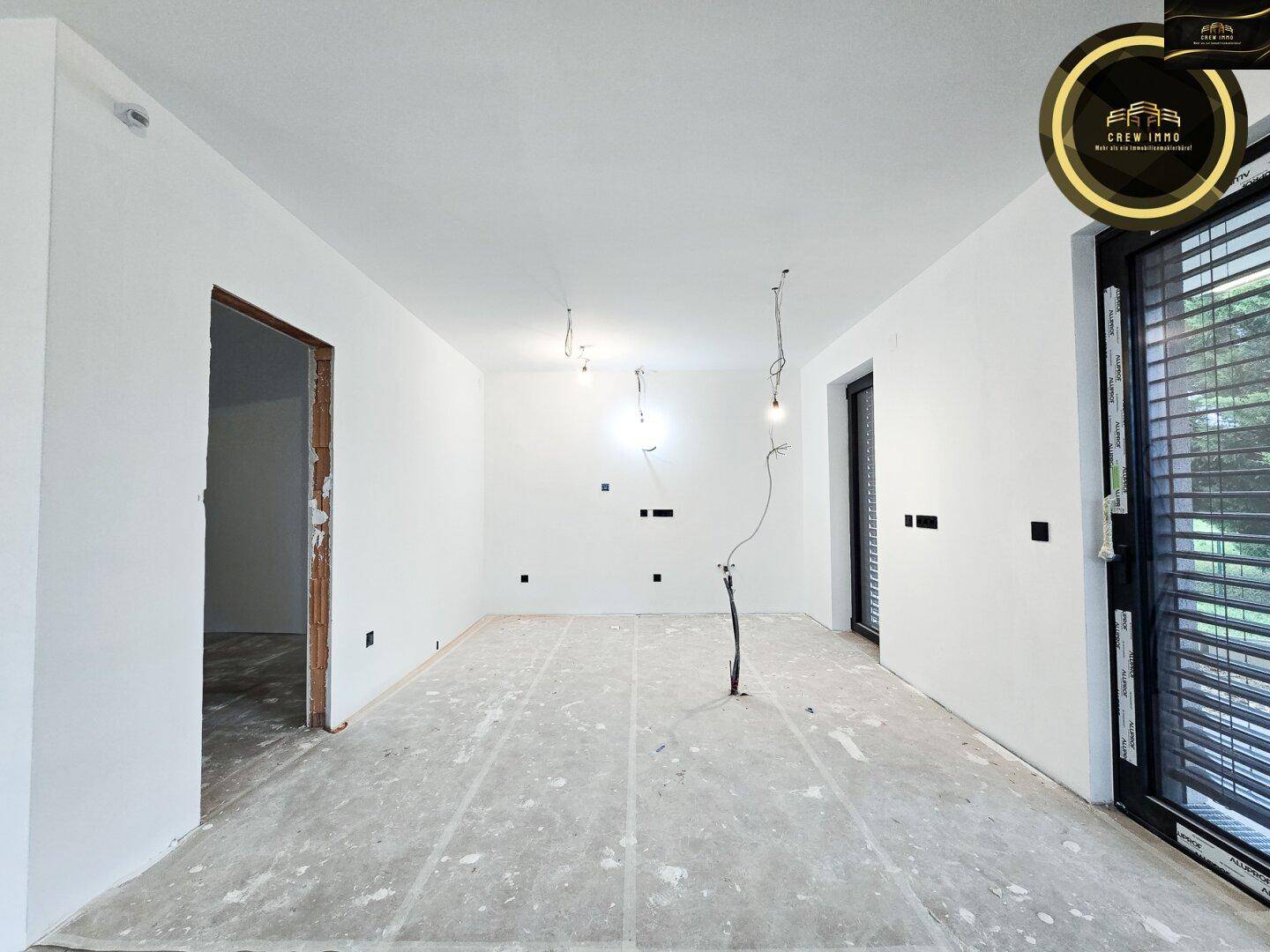 Unfertiger Küchenbereich mit rohem Boden und großen Fenstern, bereit für Einbauküche.