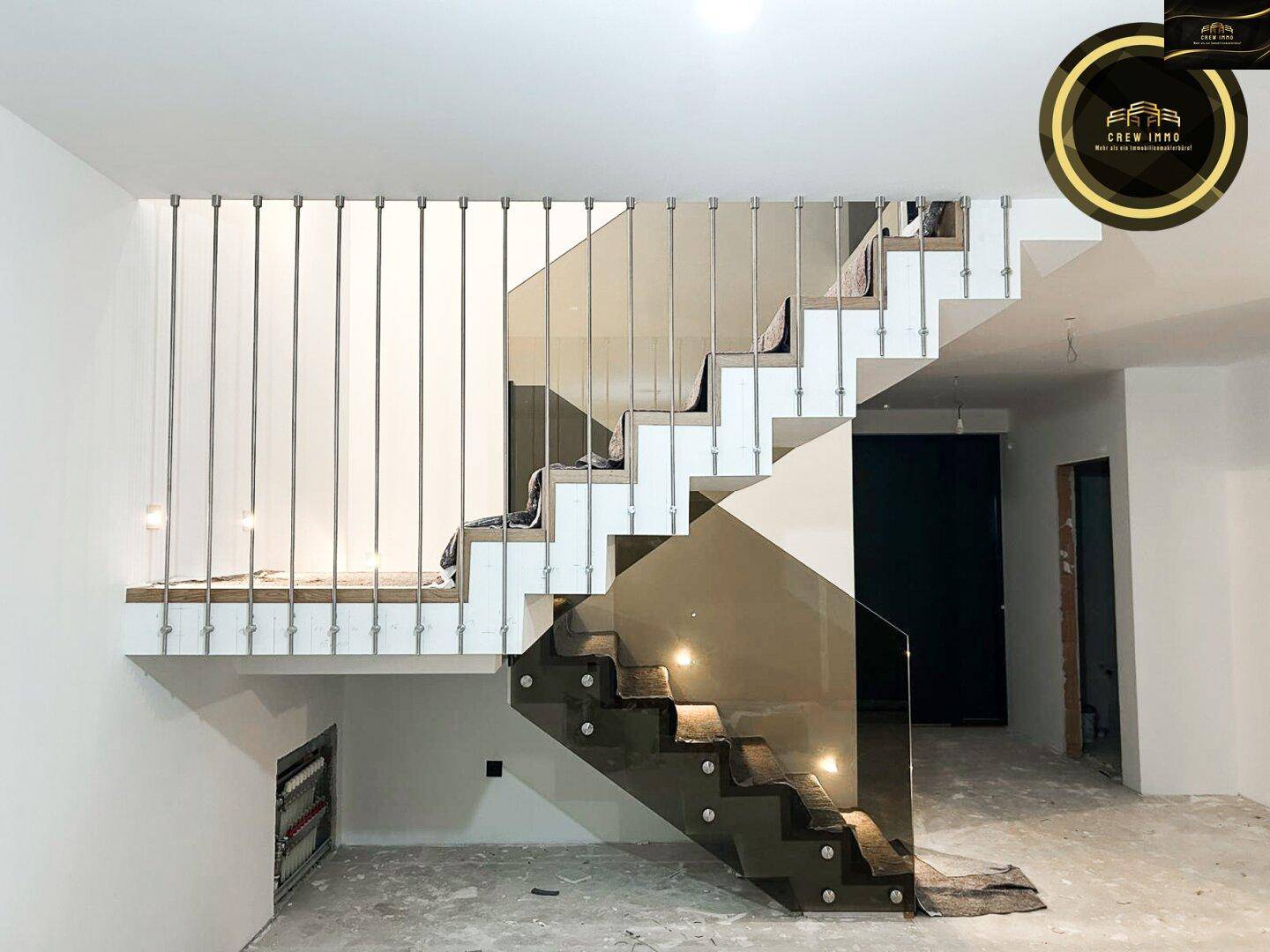 Moderne Treppe mit Teppichstufen und elegantem Glasgeländer in unfertigem Zustand.