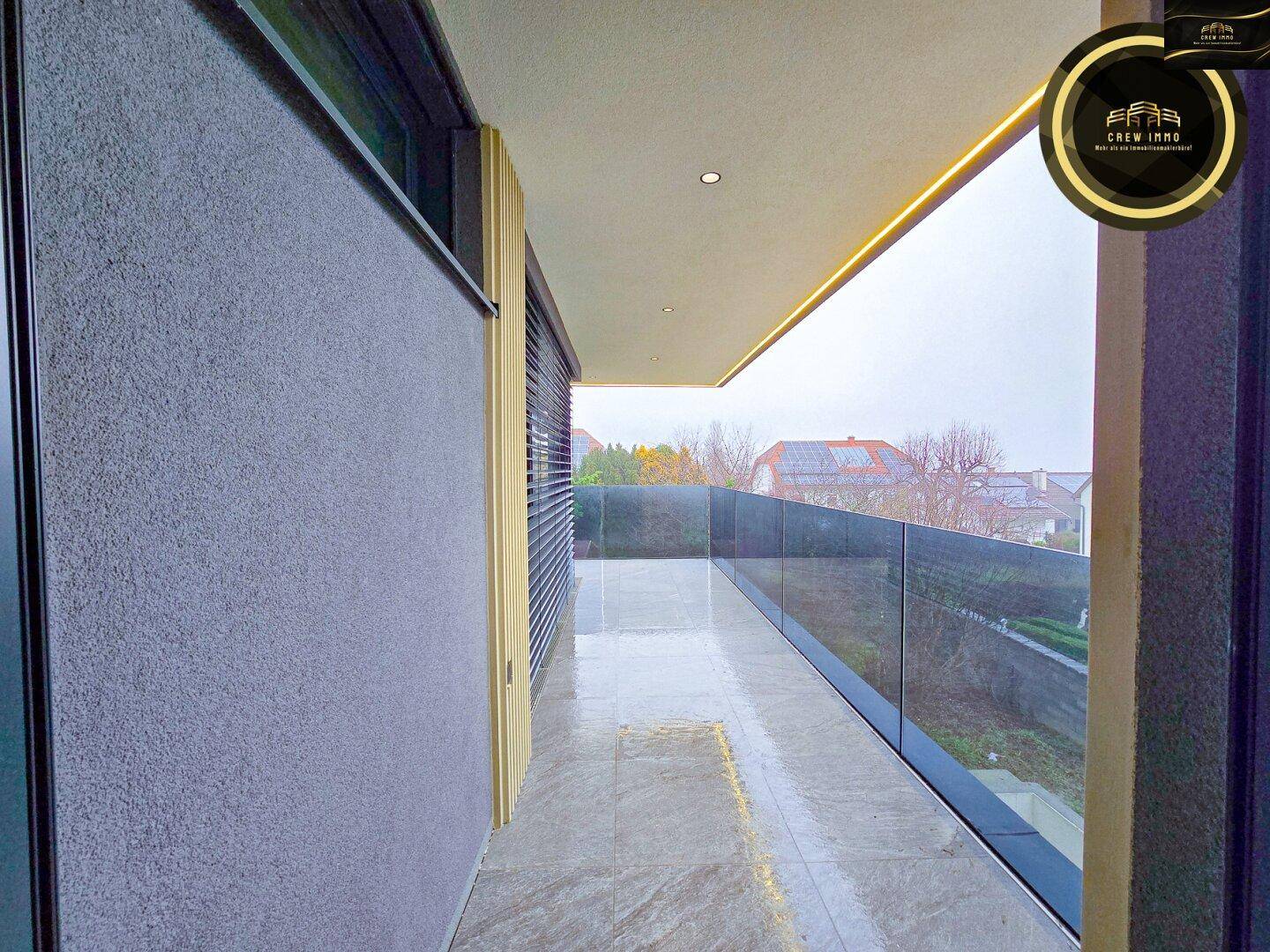 Langer, schmaler Balkon mit Glasgeländer und modernen Fliesen, ideal für Entspannung.