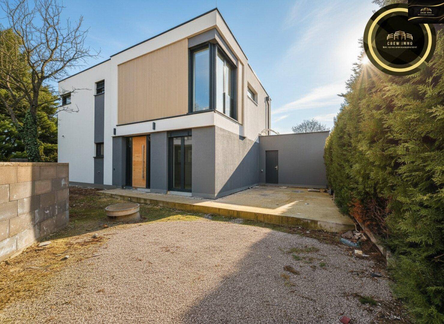 Moderne Hausfassade bei Tageslicht mit Kiesfläche und angrenzendem Gartenbereich.