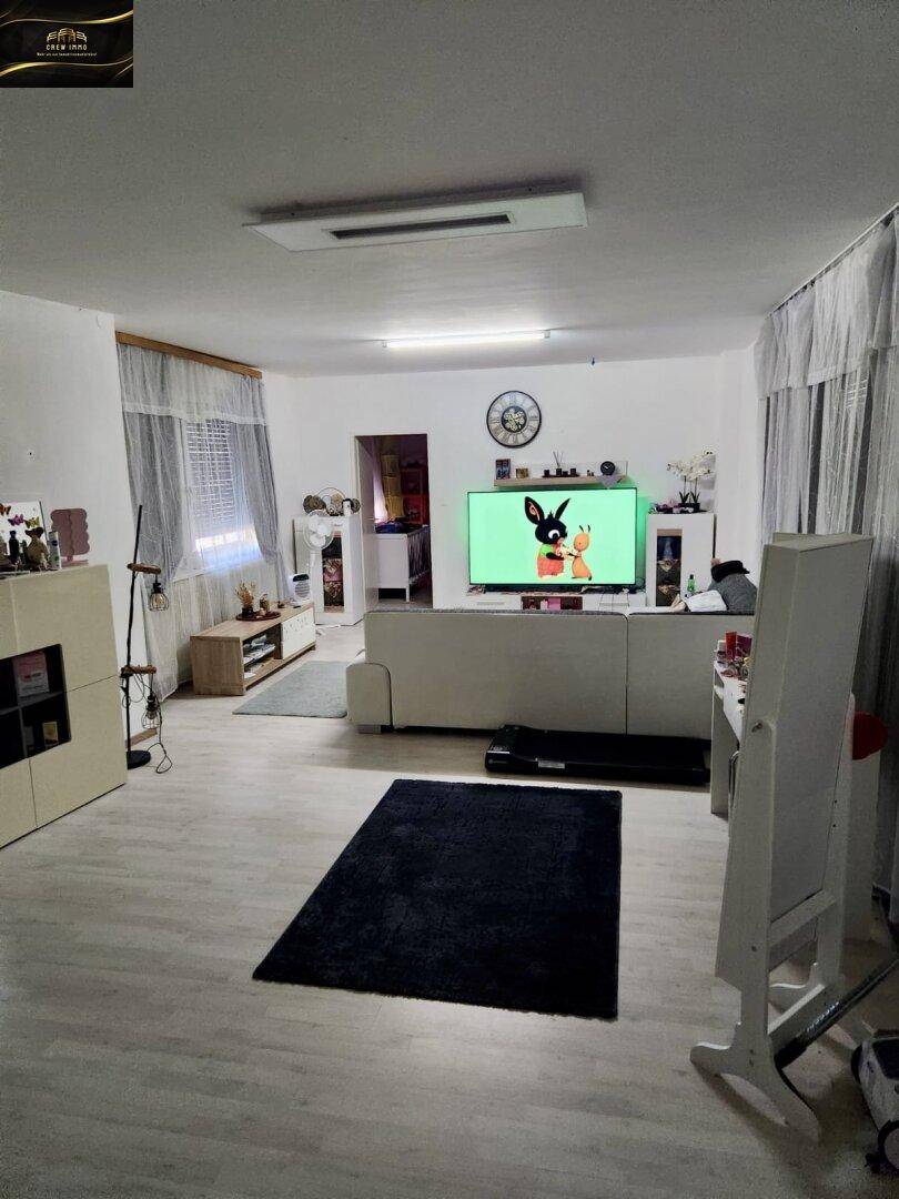 Helles Wohnzimmer mit modernem Fernseher, weißem Sofa und hellem Laminatboden.