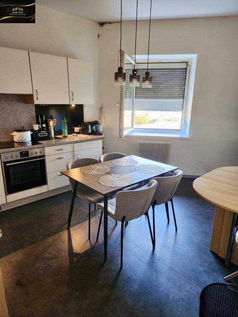 Funktionale Küche mit weißen Schränken, Esstisch und Fenster mit Rollladen.