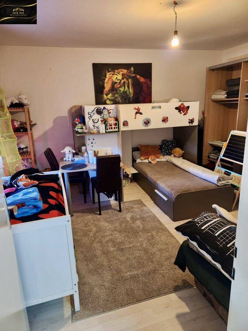 Kinderzimmer mit Etagenbett, Schreibtisch, Kleiderschrank und Teppichboden.