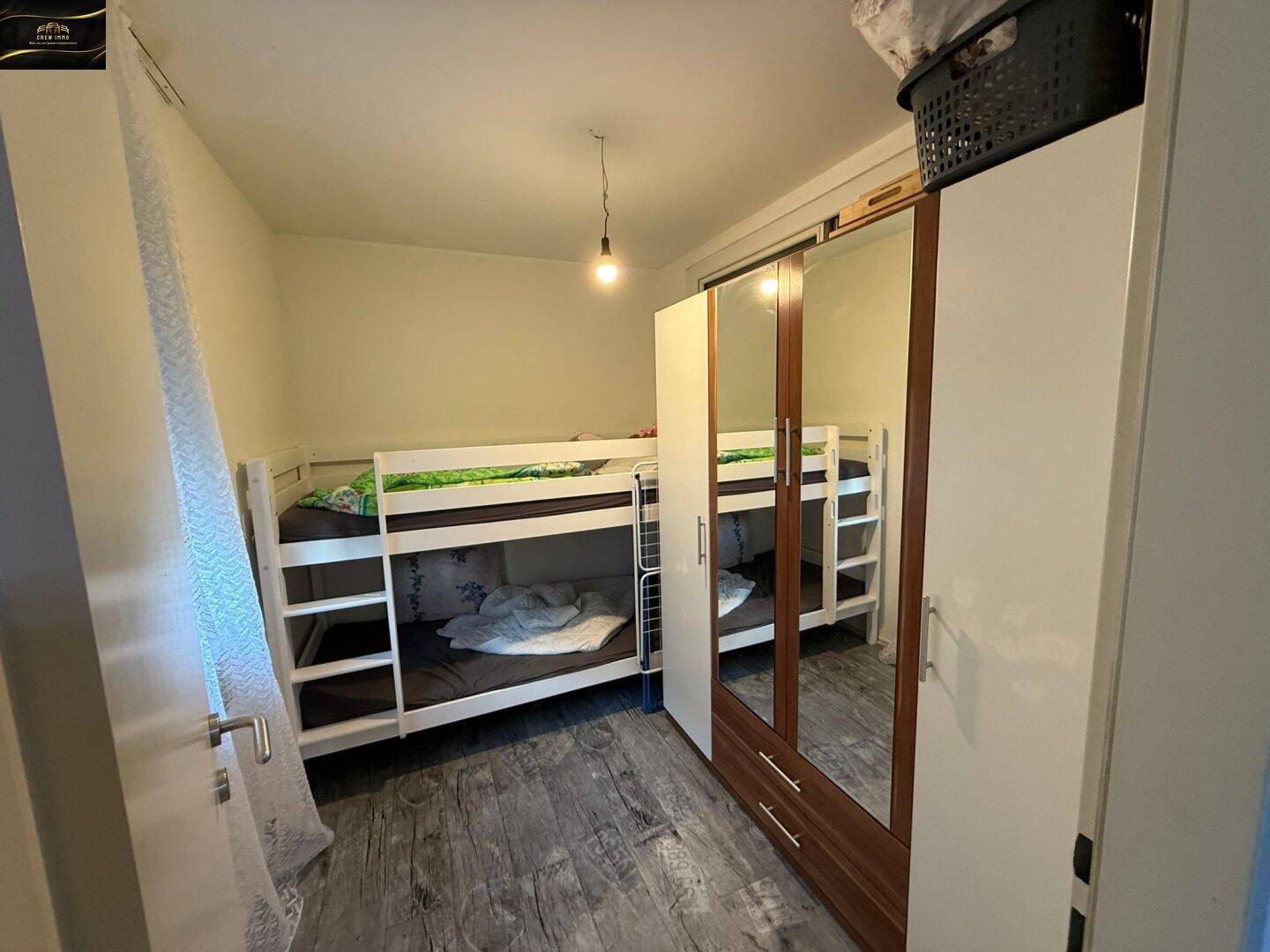 Kinderzimmer mit Etagenbetten und einem Kleiderschrank mit Spiegeltüren auf Laminatboden.