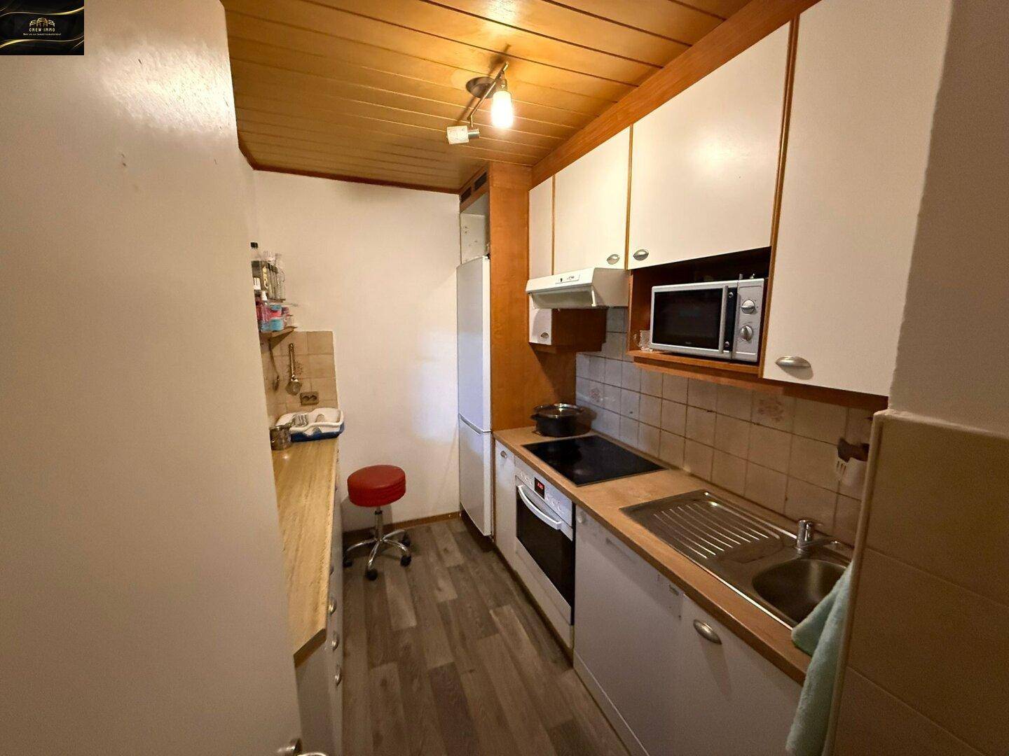 Kleine Küche mit weißen Schränken, Holzdecke und grundlegenden Küchengeräten.