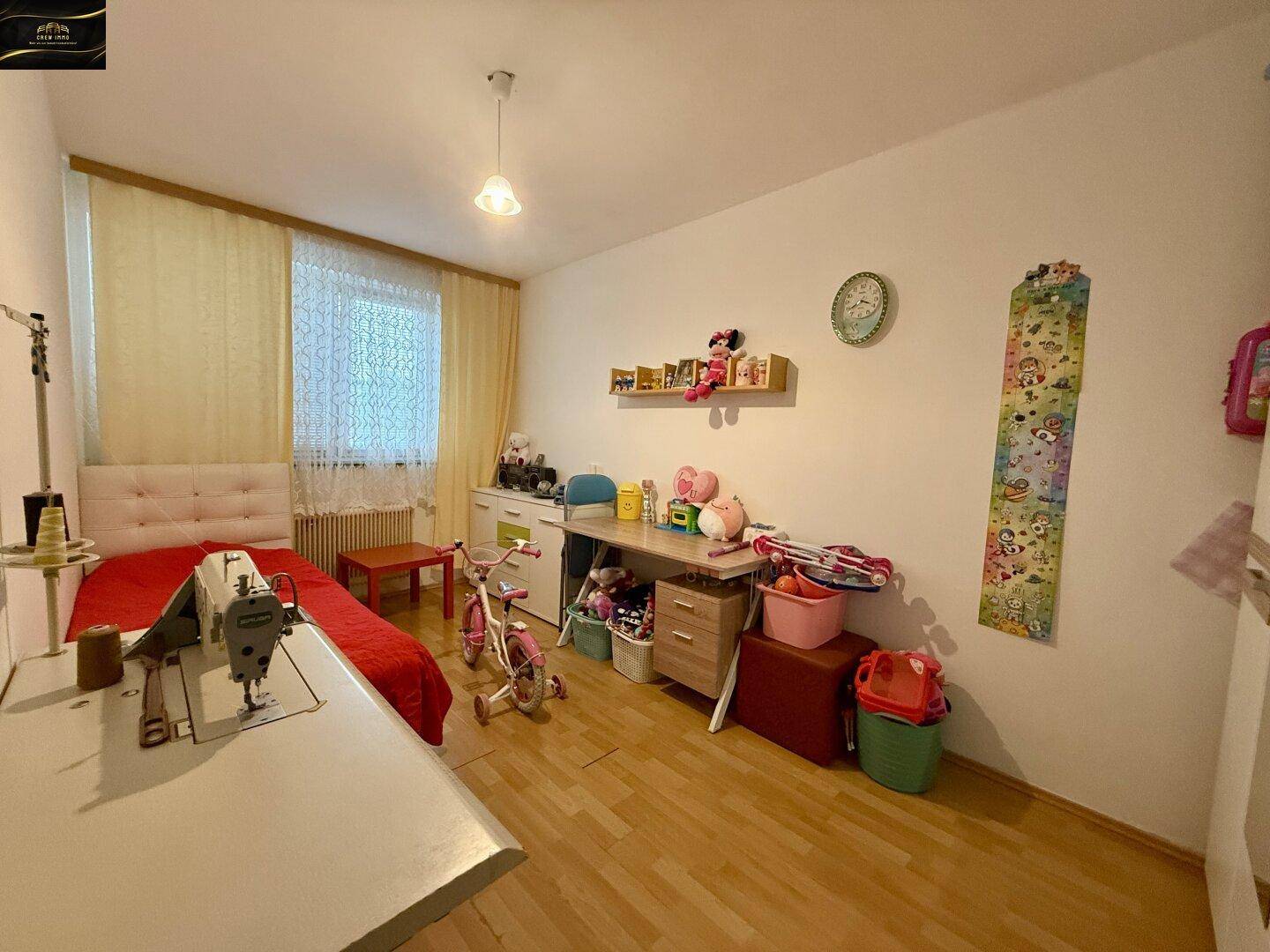 Helles Kinderzimmer mit Einzelbett, Schreibtisch und Spielzeug auf Laminatboden.