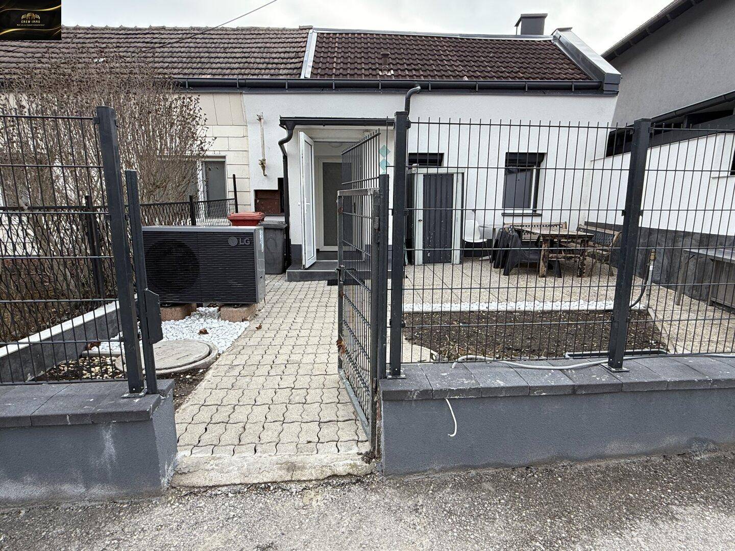 Außenansicht des Hauses mit umzäunter Terrasse und Wärmepumpe im Vorgartenbereich.