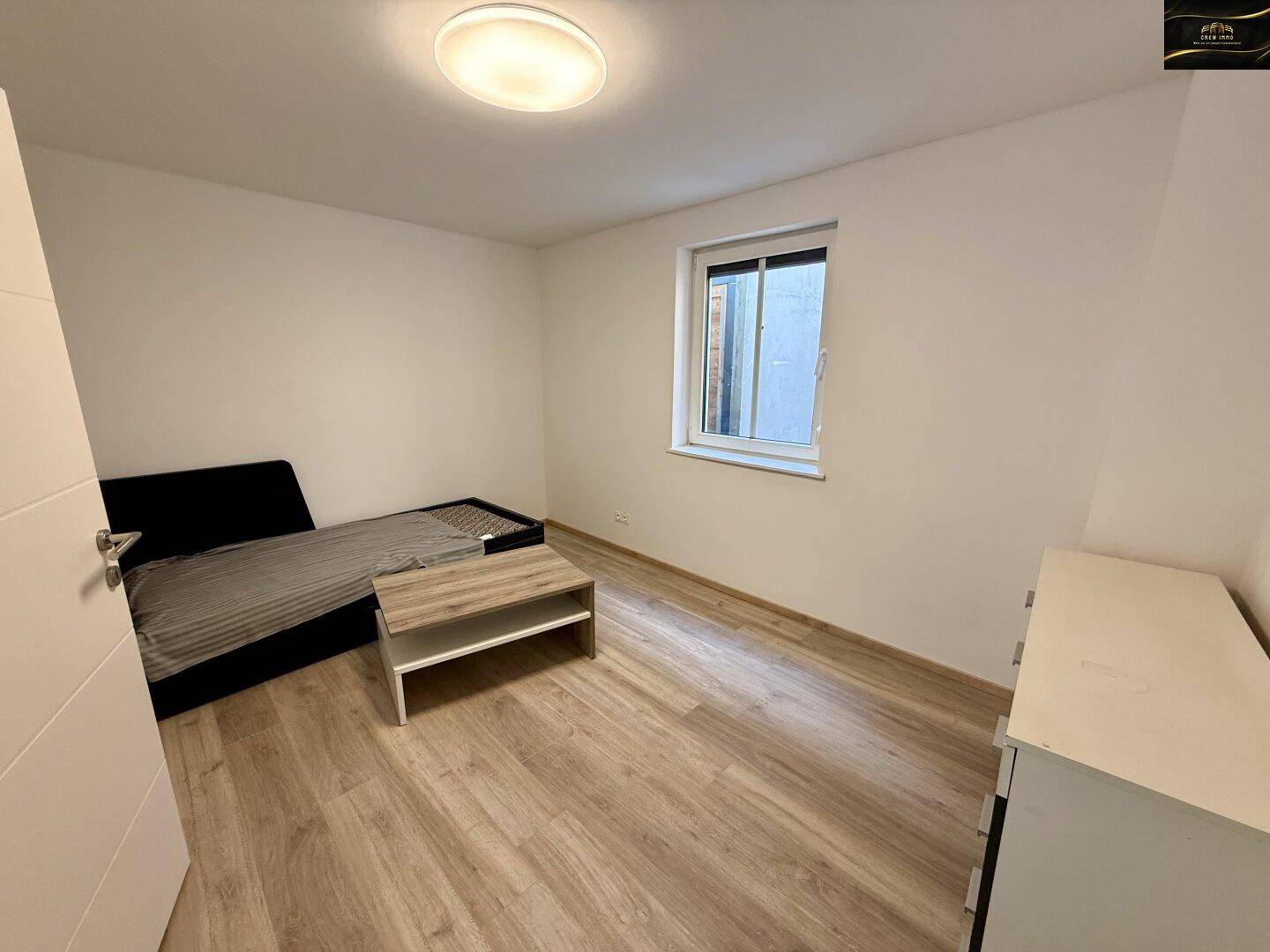 Schlafzimmer mit Laminatboden, weißen Wänden, einem Bett und einem Fenster.