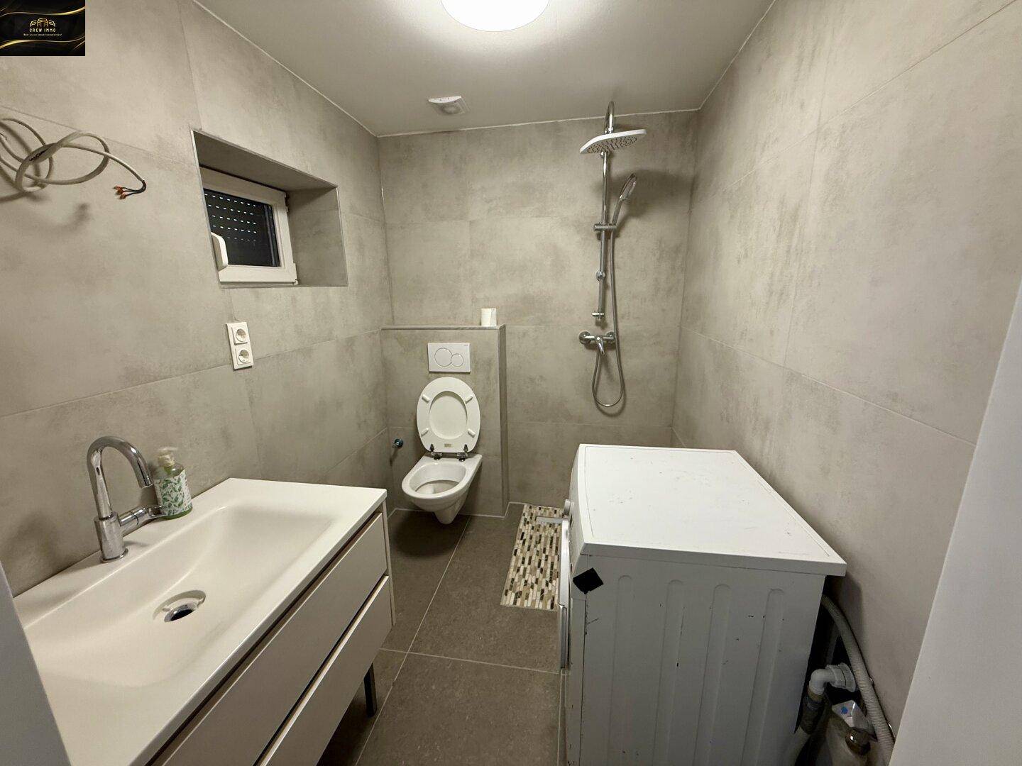 Modernes Badezimmer mit Dusche, wandhängendem WC, Waschbecken und Waschmaschine.