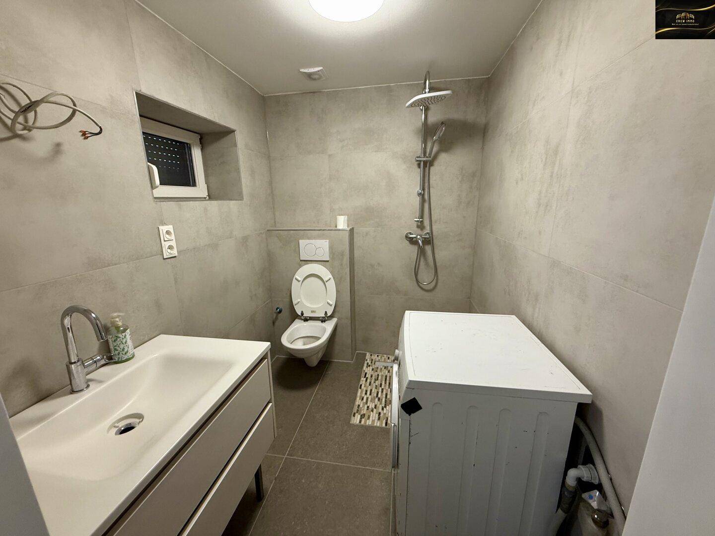Modernes Badezimmer mit Dusche, wandhängendem WC, Waschbecken und grauen Fliesen.