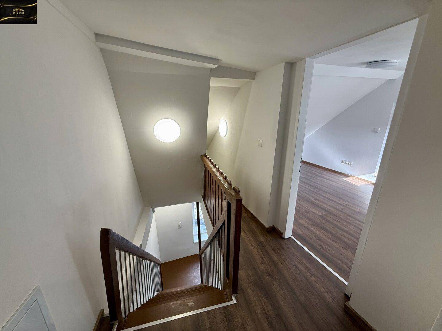 Holztreppe führt in die obere Etage, umgeben von hellen Wänden und Laminatboden.