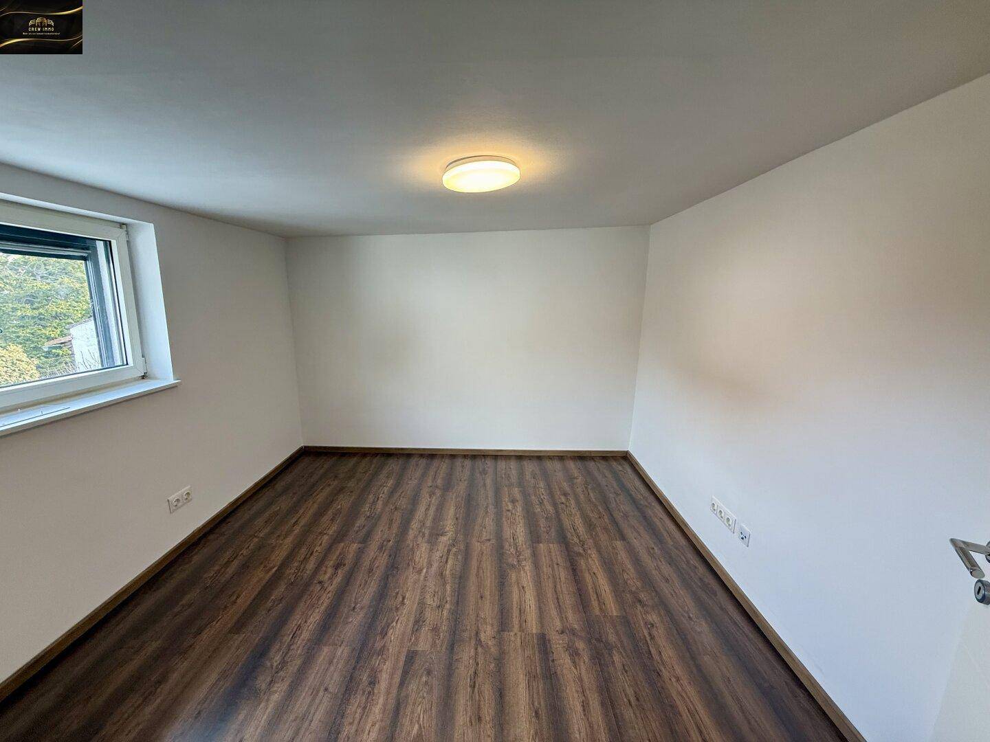 Helles Zimmer mit Laminatboden und einem Fenster, das viel Tageslicht hereinlässt.