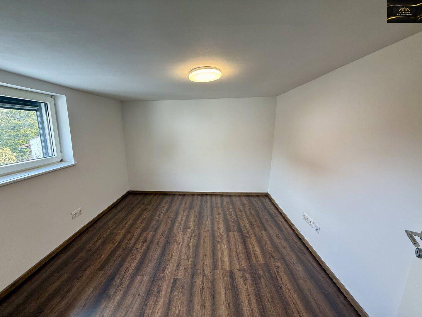 Geräumiges Zimmer mit Laminatboden, weißen Wänden und einem Fenster für natürliches Licht.