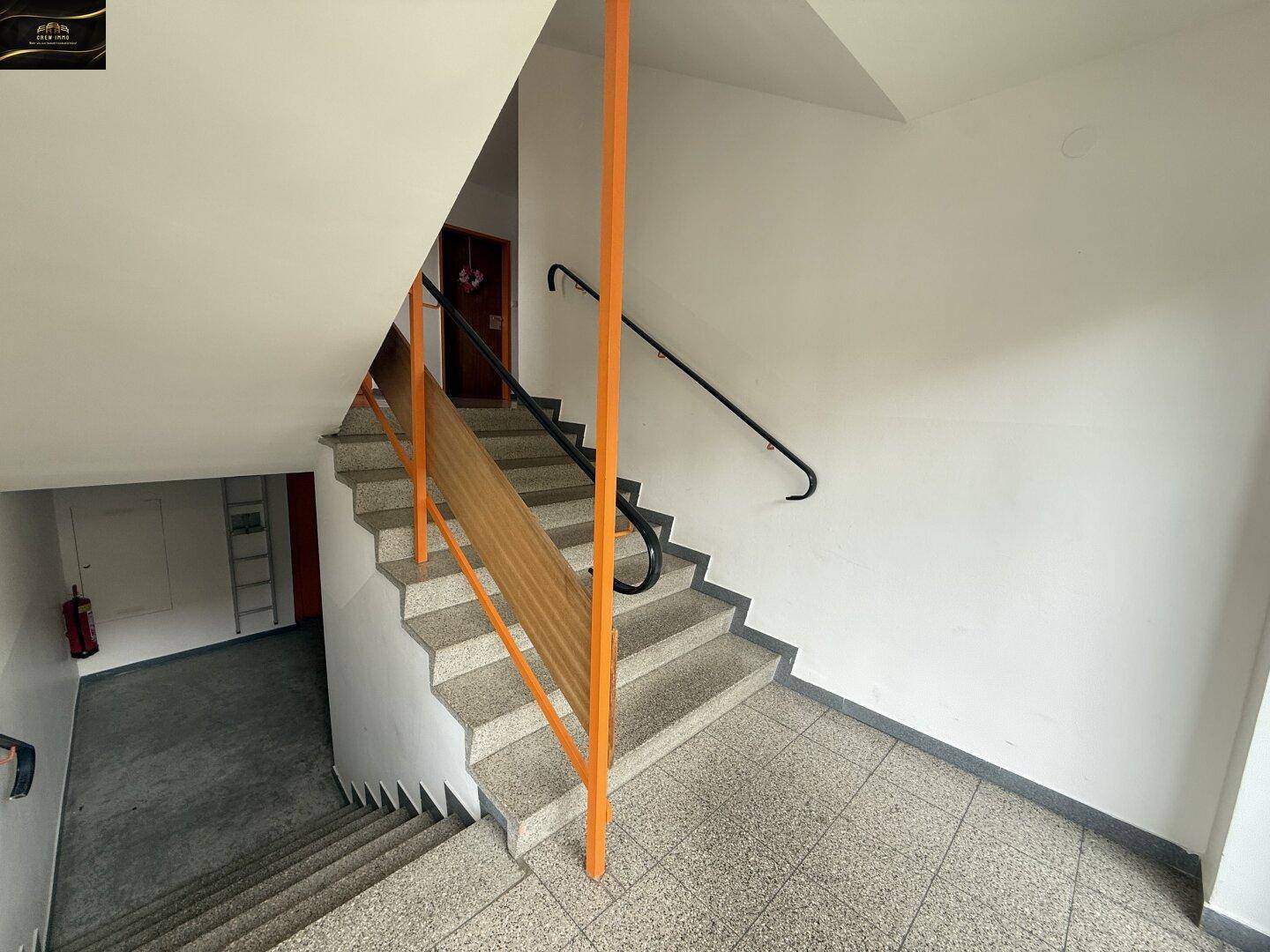 Treppenhaus mit Terrazzoboden und orangefarbenem Geländer in einem Mehrfamilienhaus.