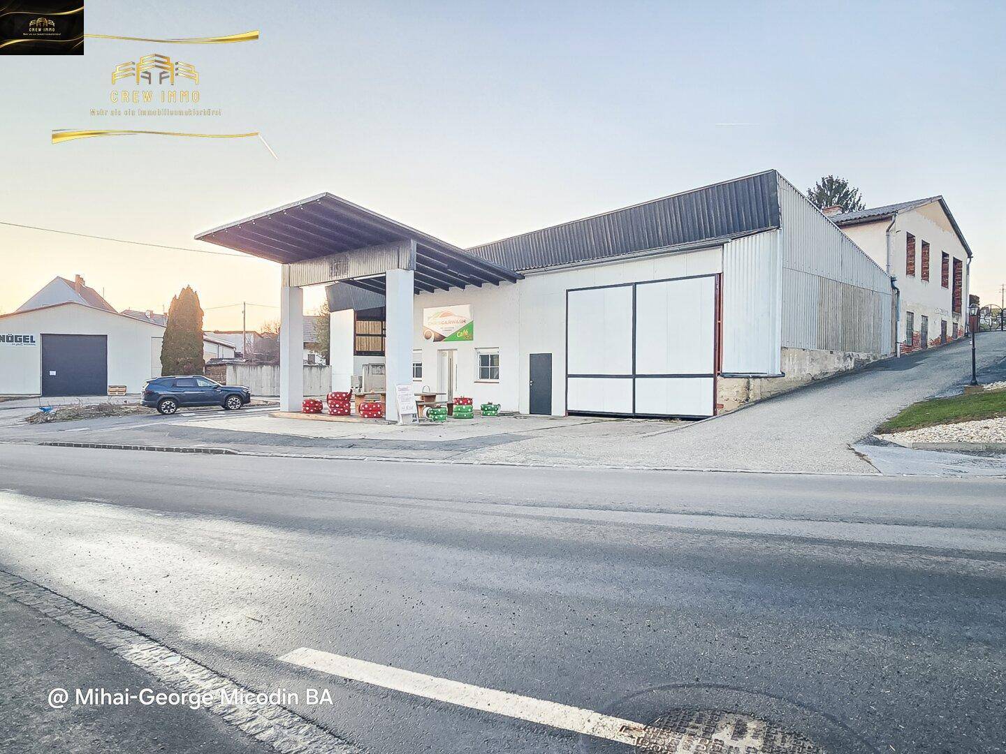 Gesamtansicht des Gebäudes mit überdachtem Bereich und angrenzendem Parkplatz für Fahrzeuge.
