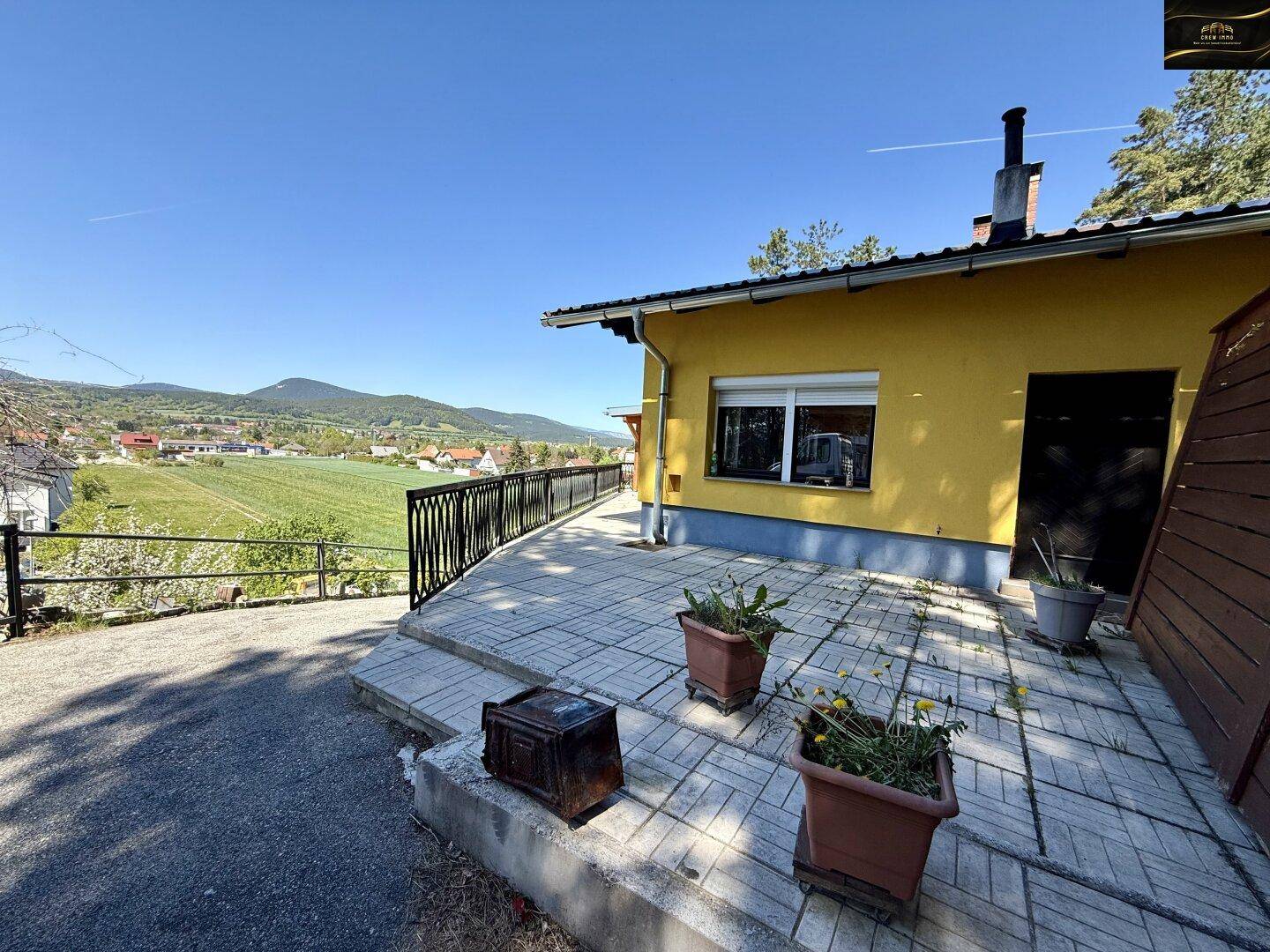 Sonnige Terrasse am Haus mit gepflastertem Boden, Geländer und weitem Blick auf die grüne Landschaft.