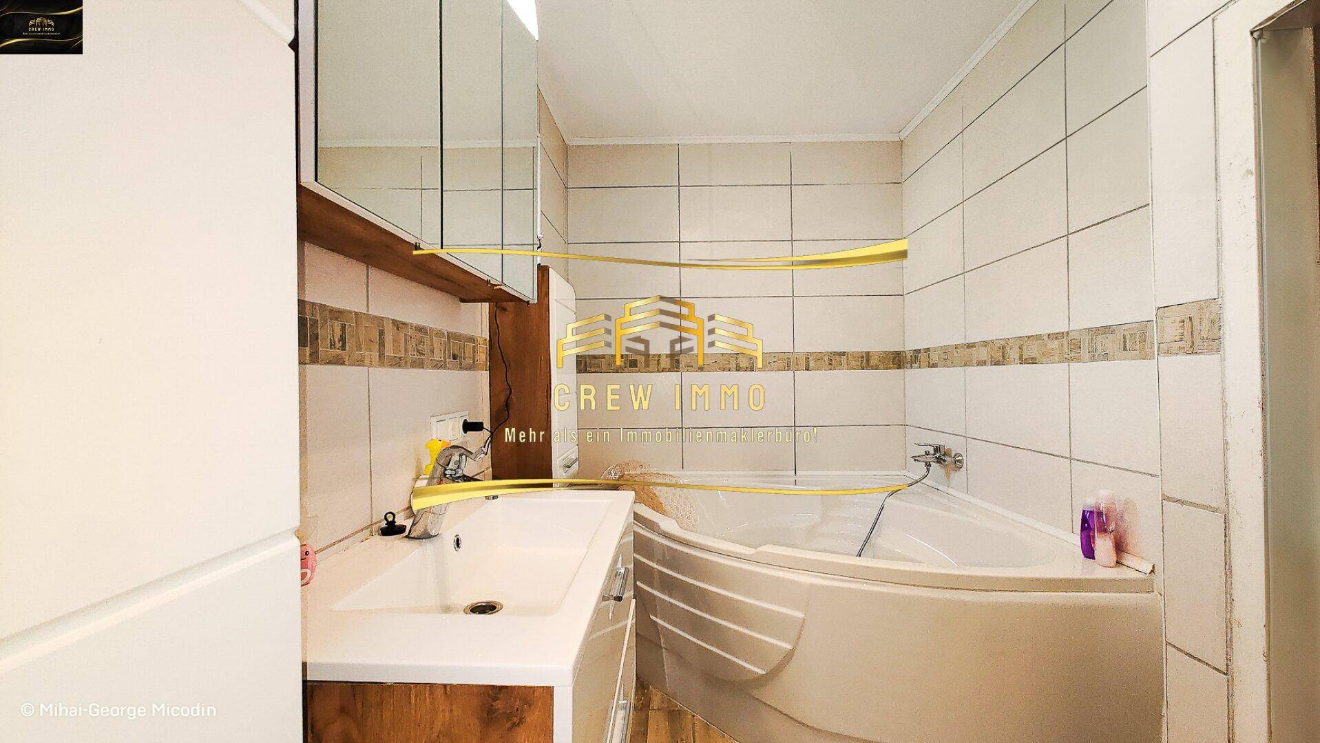 Badezimmer mit Eckbadewanne, Waschbecken und hellen Fliesen an den Wänden.