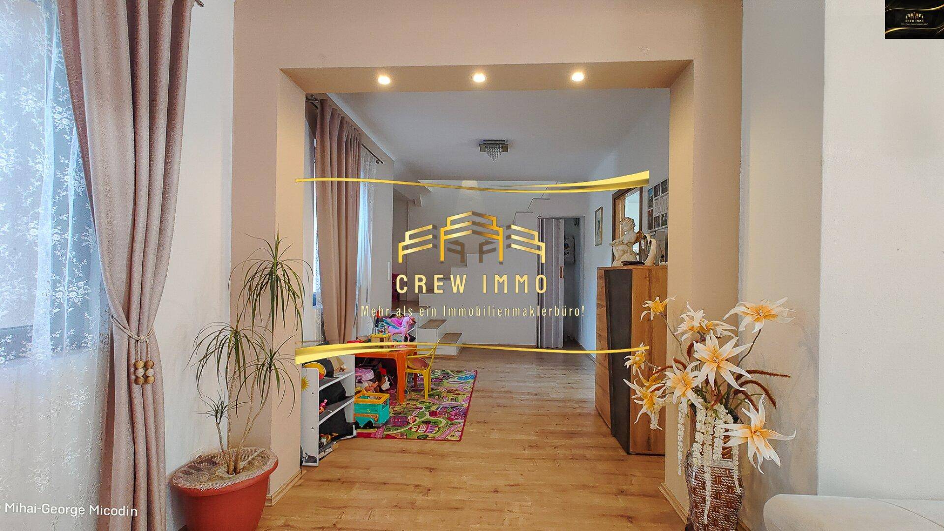Heller Durchgangsbereich mit Holzboden, der zu einem weiteren Zimmer mit Kinderspielzeug führt.