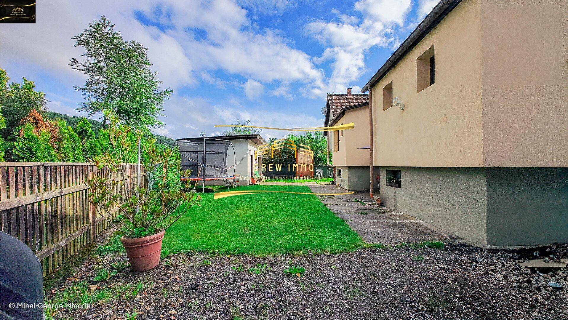 Hinterhof mit Rasenfläche, Trampolin und Blick auf die Rückseite des Hauses.