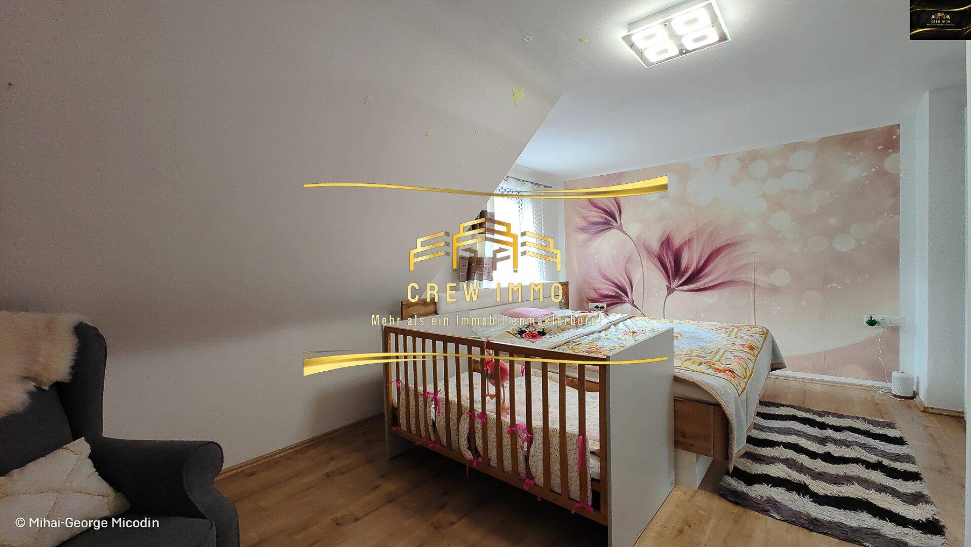 Helles Schlafzimmer mit Dachschräge, Kinderbett und einem bequemen Sessel, ideal für Familien.