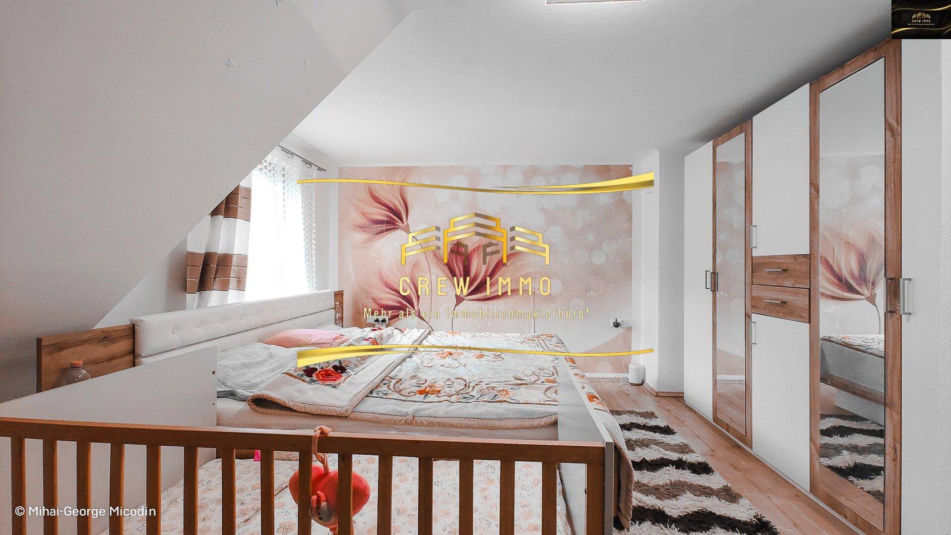 Gemütliches Schlafzimmer mit Dachschräge, Kinderbett, großem Spiegelschrank und floraler Tapete.