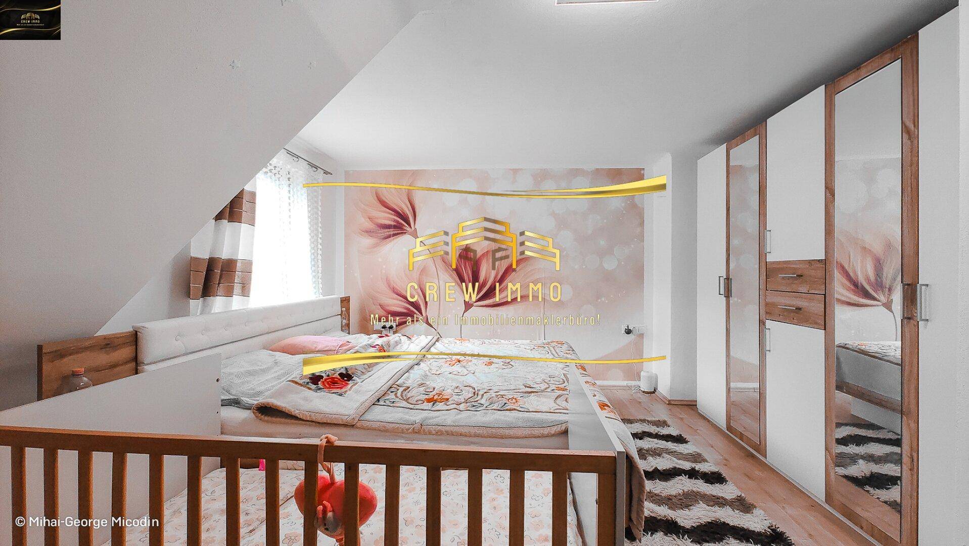 Gemütliches Schlafzimmer im Dachgeschoss mit schräger Decke, großem Bett und Spiegelschränken.