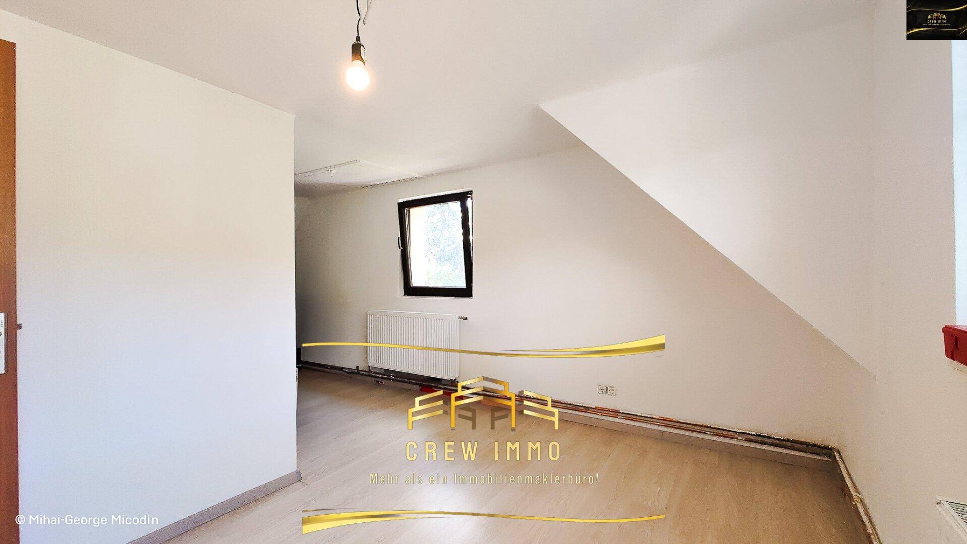 Leeres Zimmer mit Dachschräge, Fenster und Heizkörper, bereit zur individuellen Gestaltung.