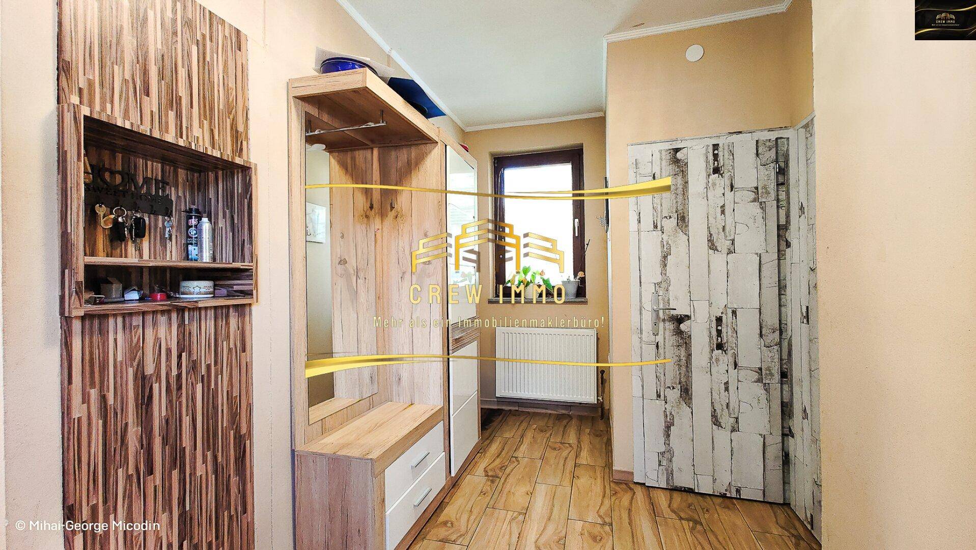 Eingangsbereich mit Garderobe aus Holz, Spiegel und einem Fenster für natürliches Licht.