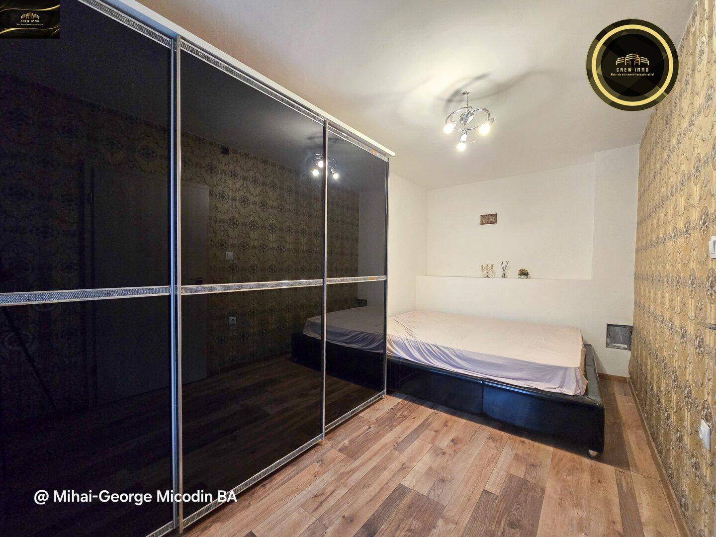 Schlafzimmer mit großem Kleiderschrank, Holzboden und gemusterter Tapete.