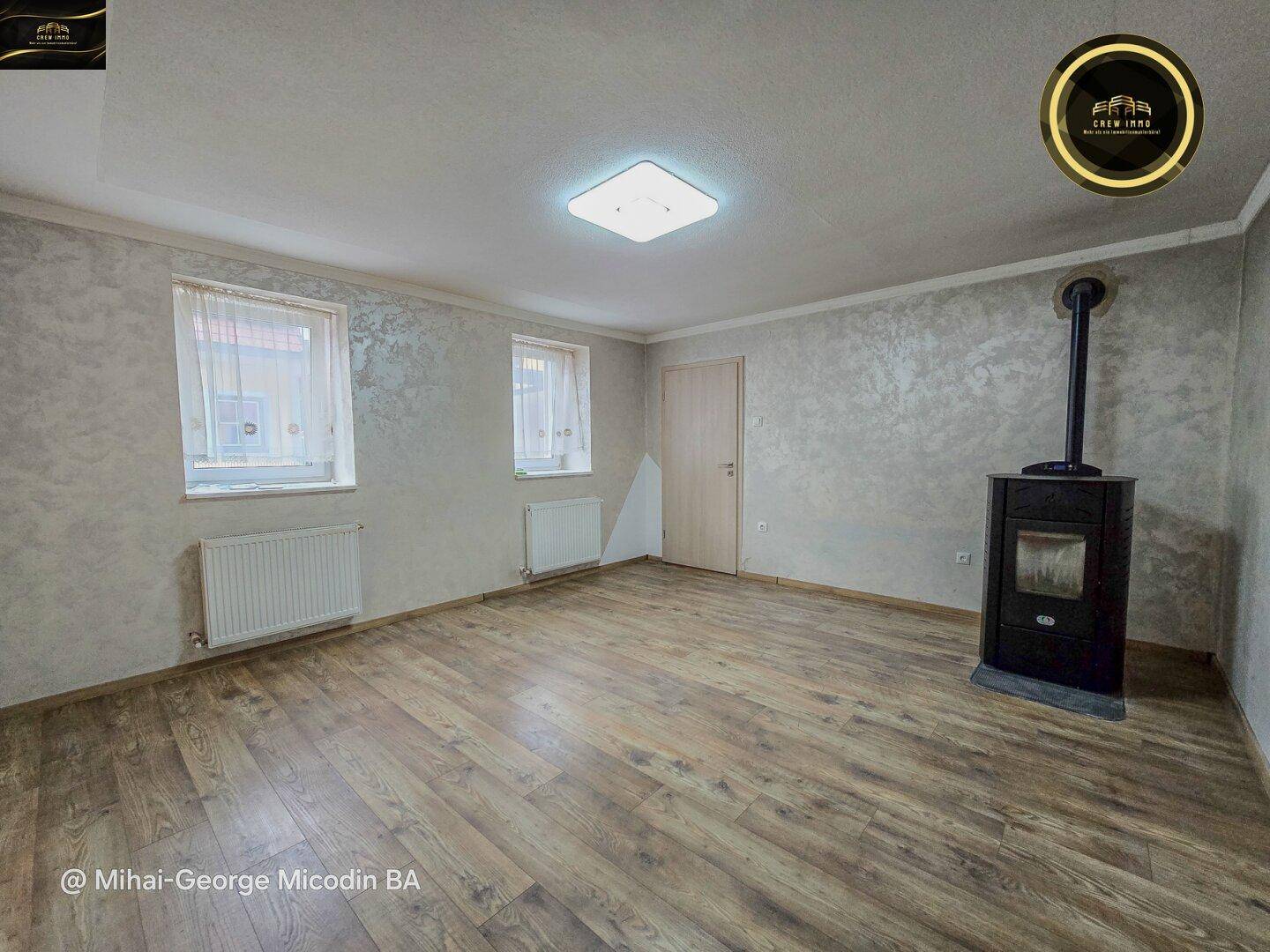 Geräumiges Wohnzimmer mit Holzboden, strukturierten Wänden und einem Holzofen.