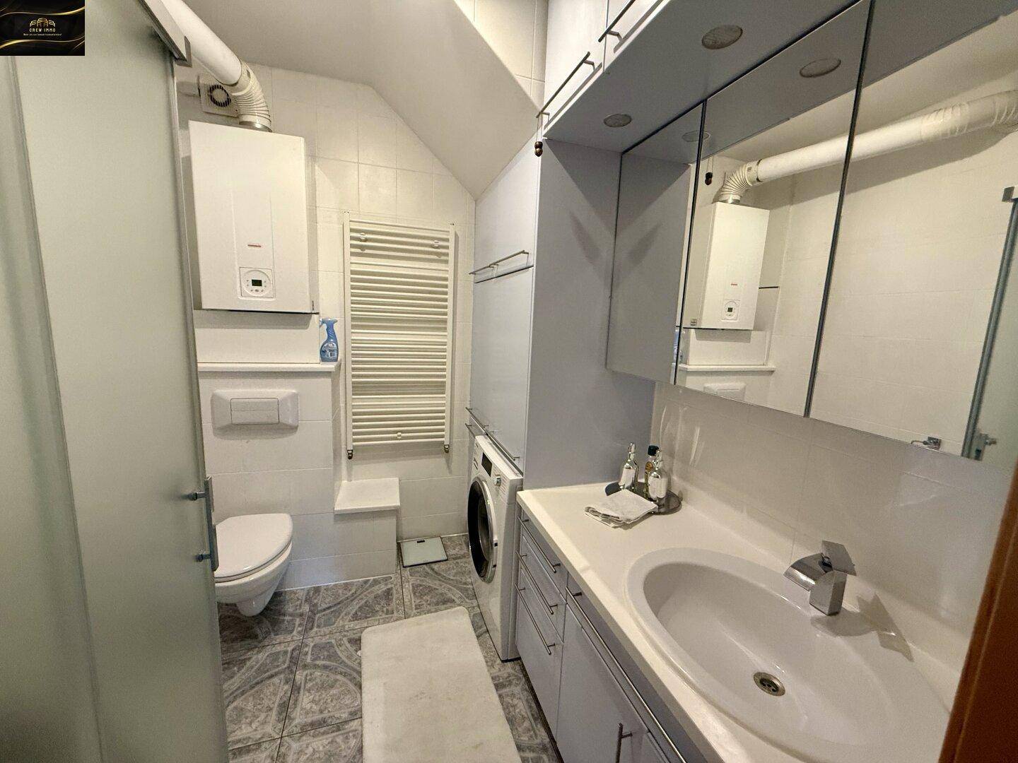 Badezimmer mit Dusche, Waschbecken, Toilette und Waschmaschine unter der Dachschräge.