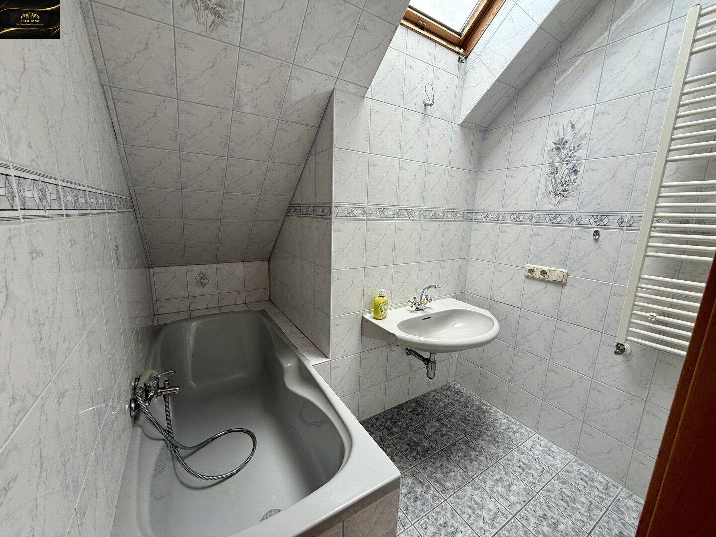 Badezimmer im Dachgeschoss mit Badewanne, Waschbecken, Toilette und Dachfenster.