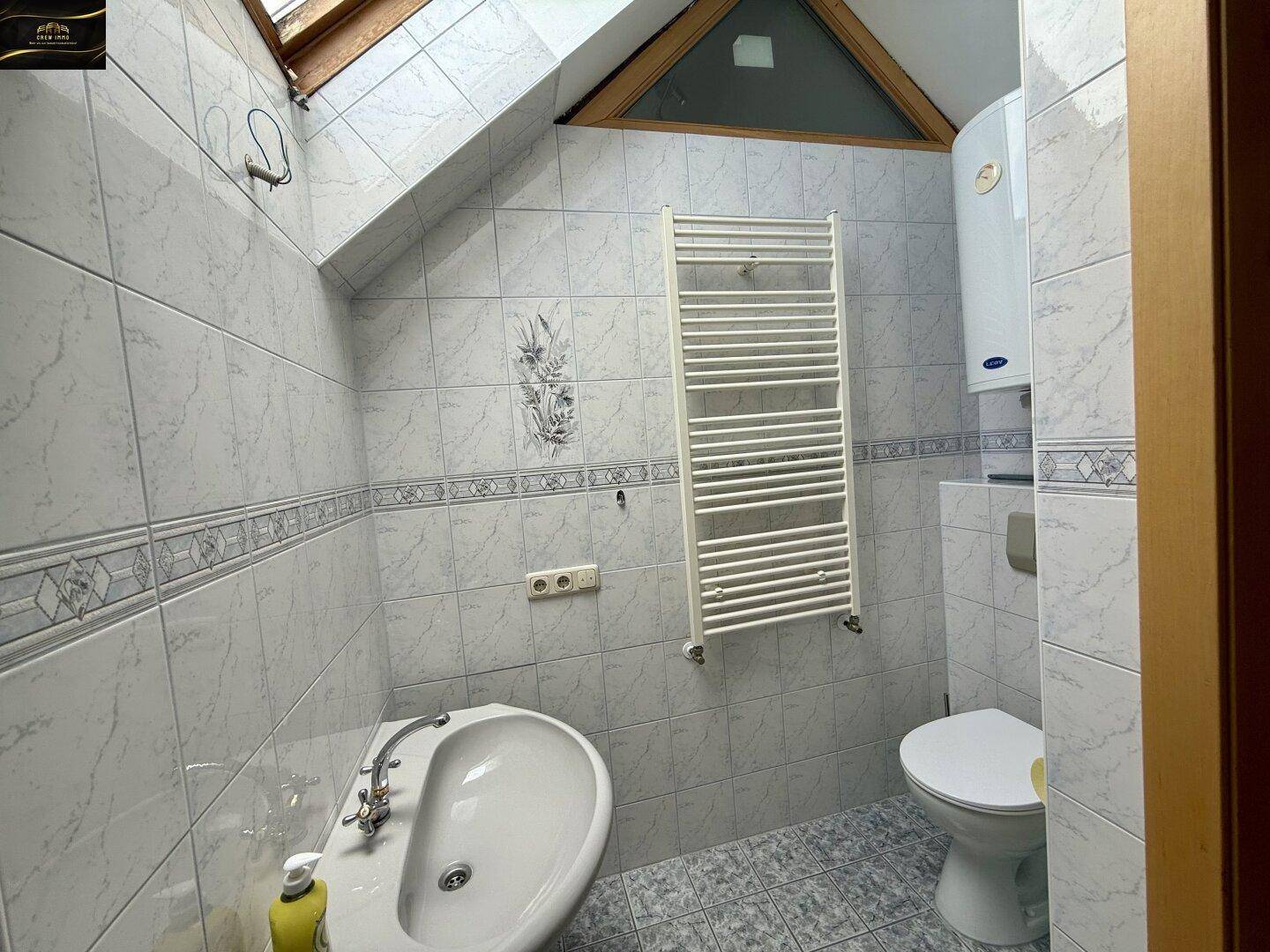 Badezimmer im Dachgeschoss mit Waschbecken, Toilette, Heizkörper und Dachfenster.