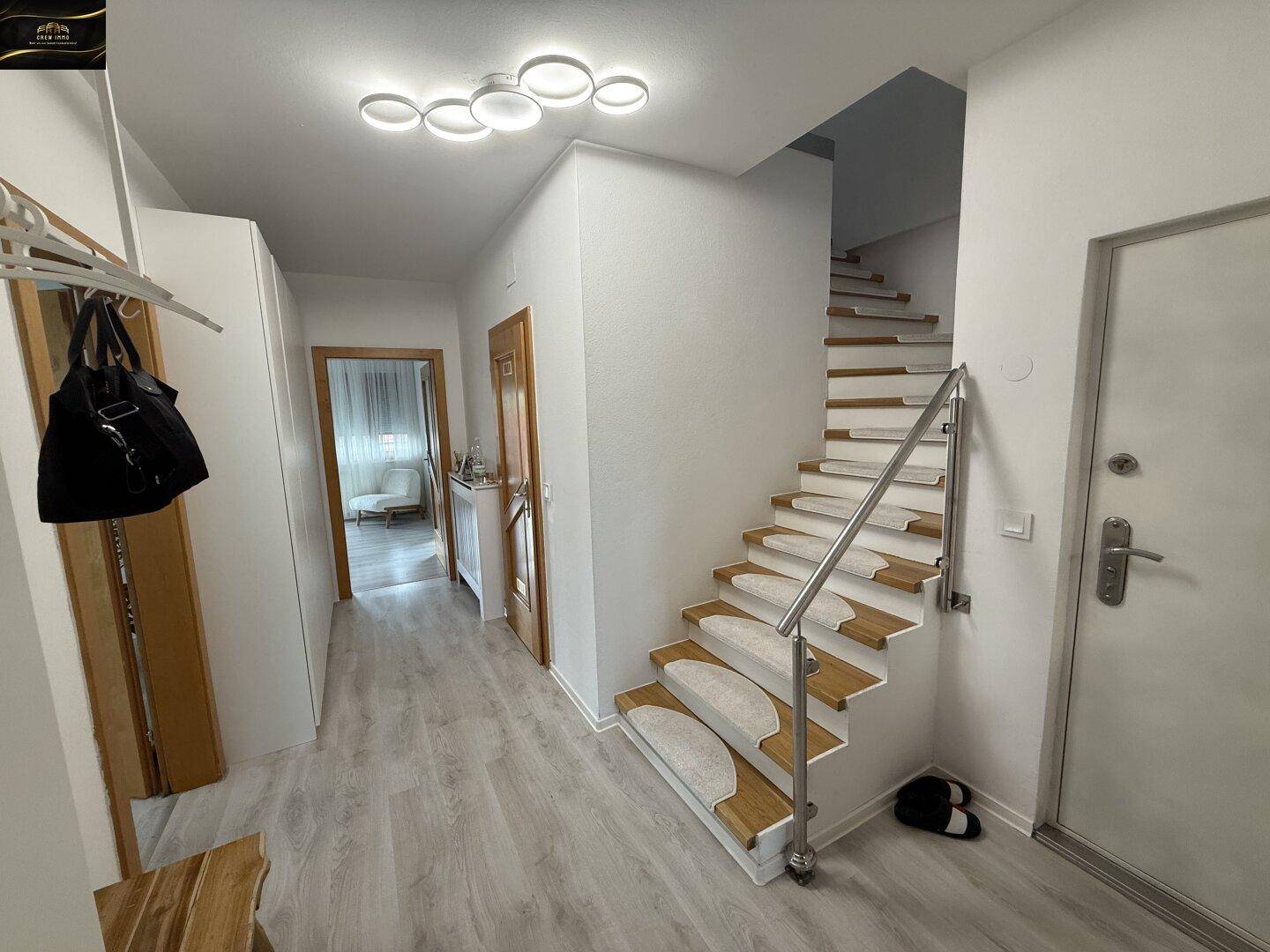 Heller Eingangsbereich mit Treppe, Garderobe und Laminatboden, der zu weiteren Räumen führt.