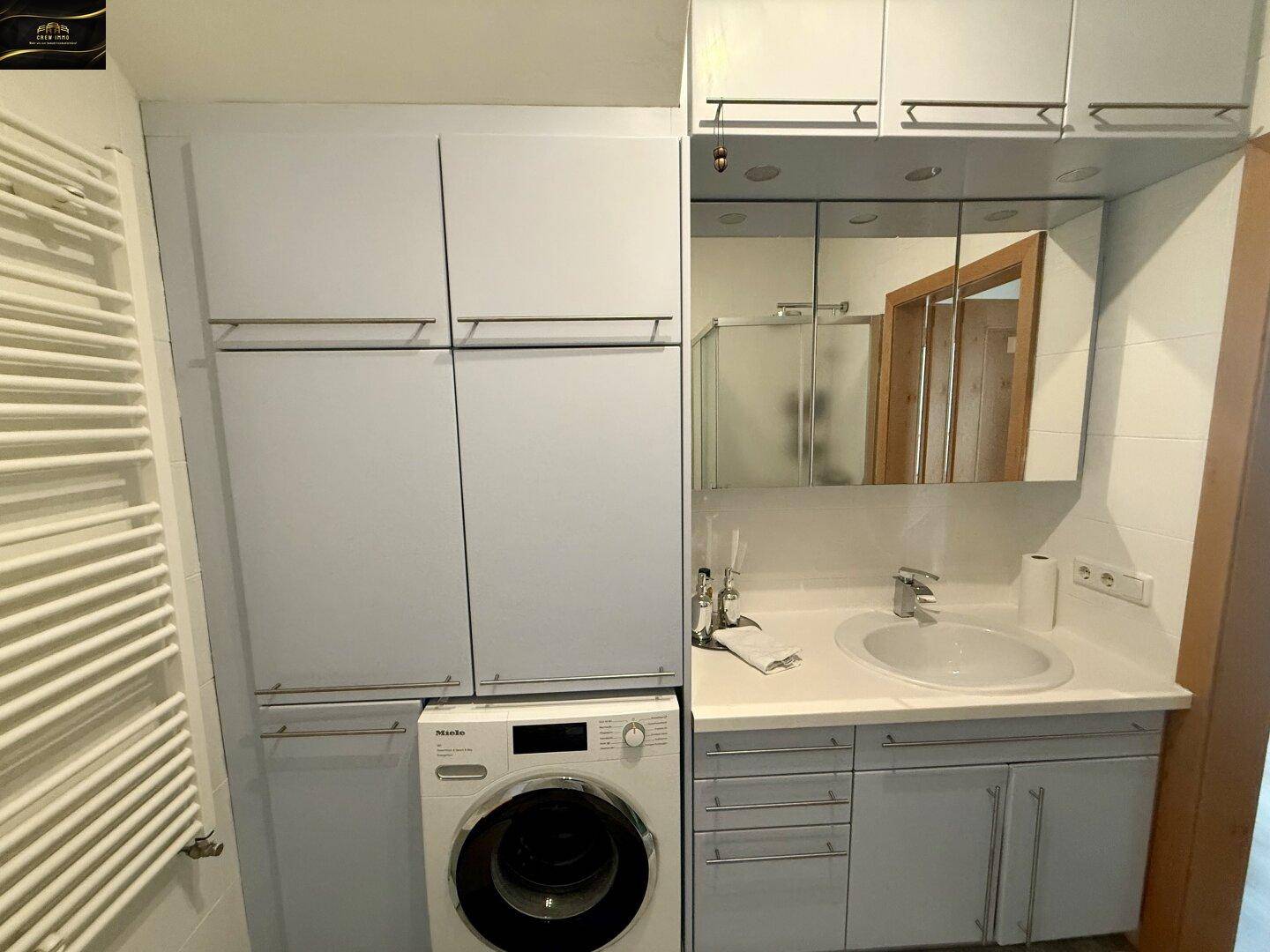 Badezimmer mit Waschbecken, Spiegelschrank, Waschmaschine und Heizkörper.