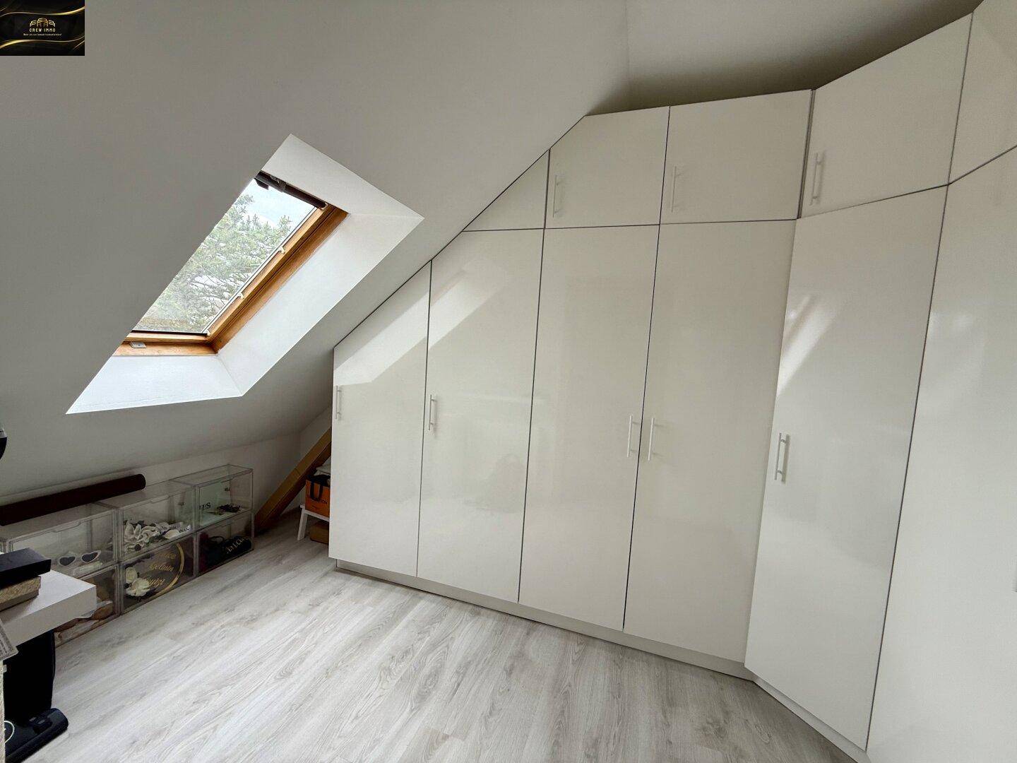 Dachgeschossraum mit glänzenden weißen Einbauschränken und Dachfenster für natürliches Licht.