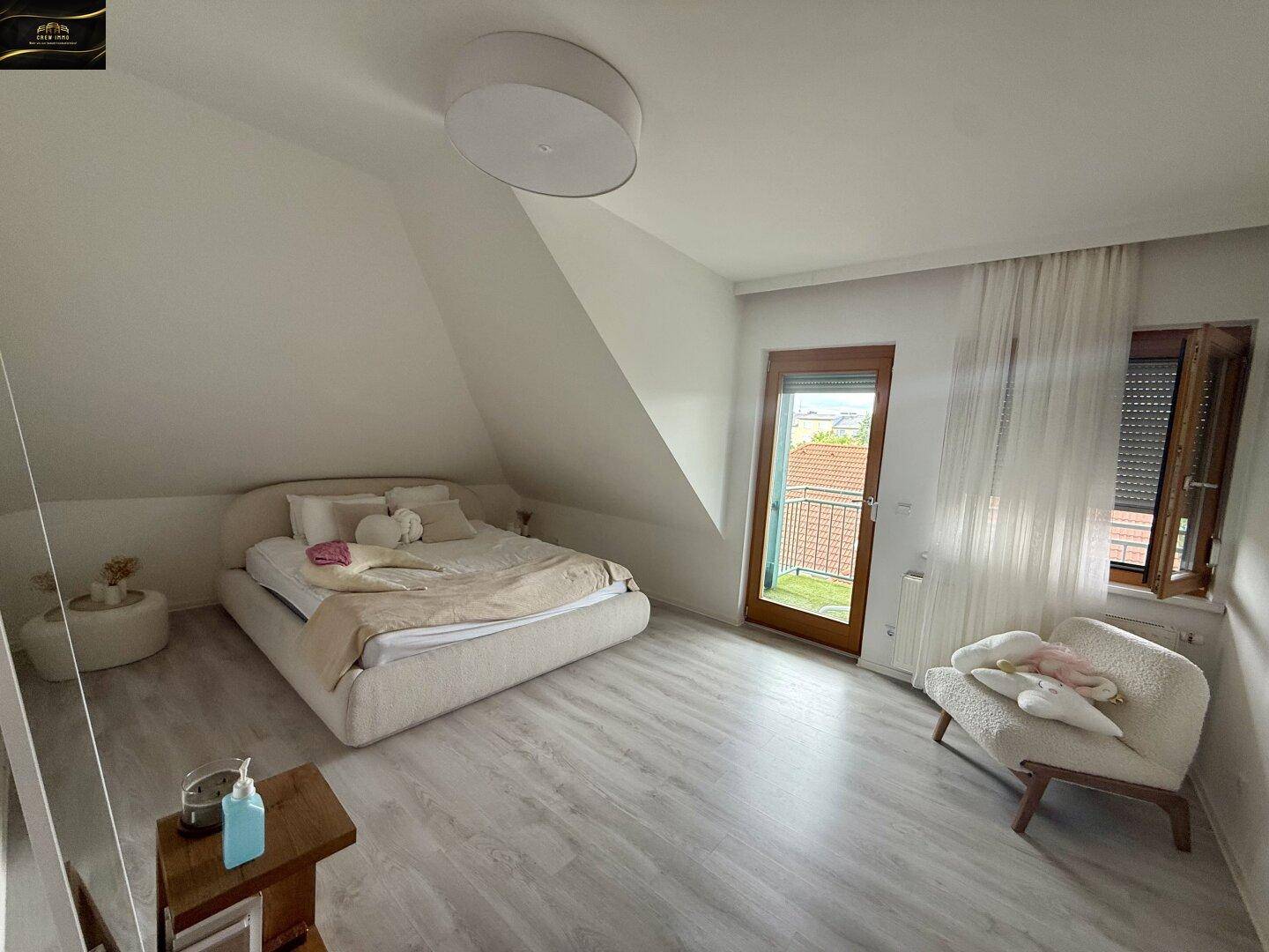 Helles Schlafzimmer im Dachgeschoss mit Doppelbett, schräger Decke und Zugang zum Balkon.