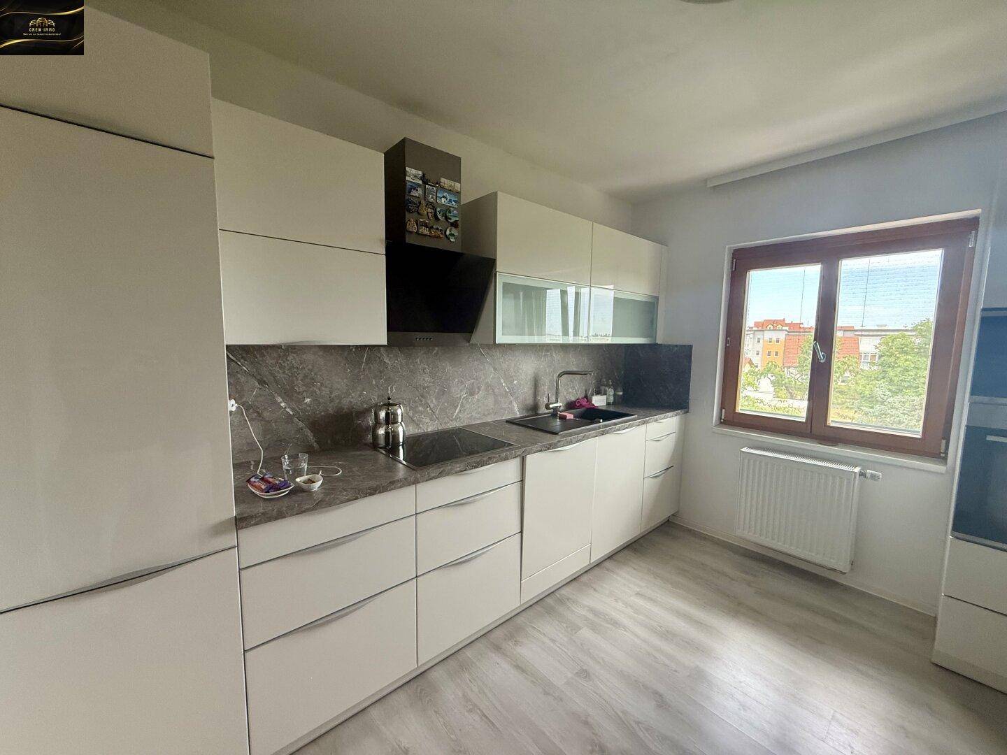 Moderne Einbauküche mit weißen Schränken, dunkler Arbeitsplatte und Fenster mit Blick ins Grüne.