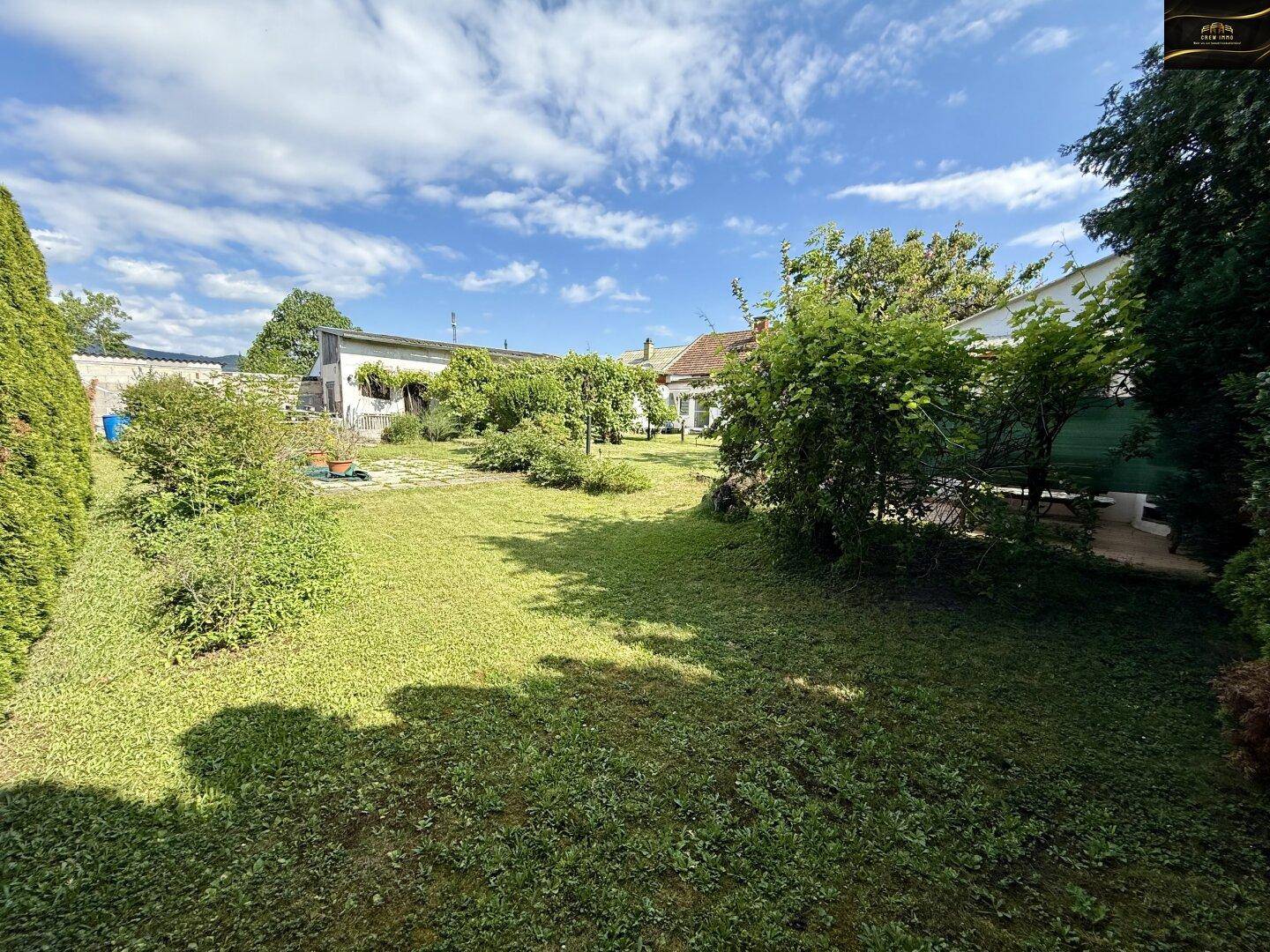 Weitläufiger grüner Garten mit Bäumen und Sträuchern unter einem blauen Himmel.