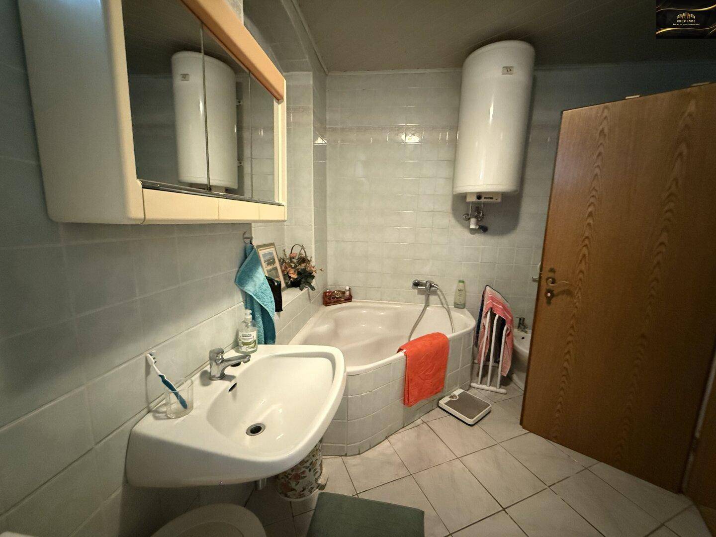 Badezimmer mit Eckbadewanne, Waschbecken, Spiegelschrank und Fliesen an Wänden und Boden.